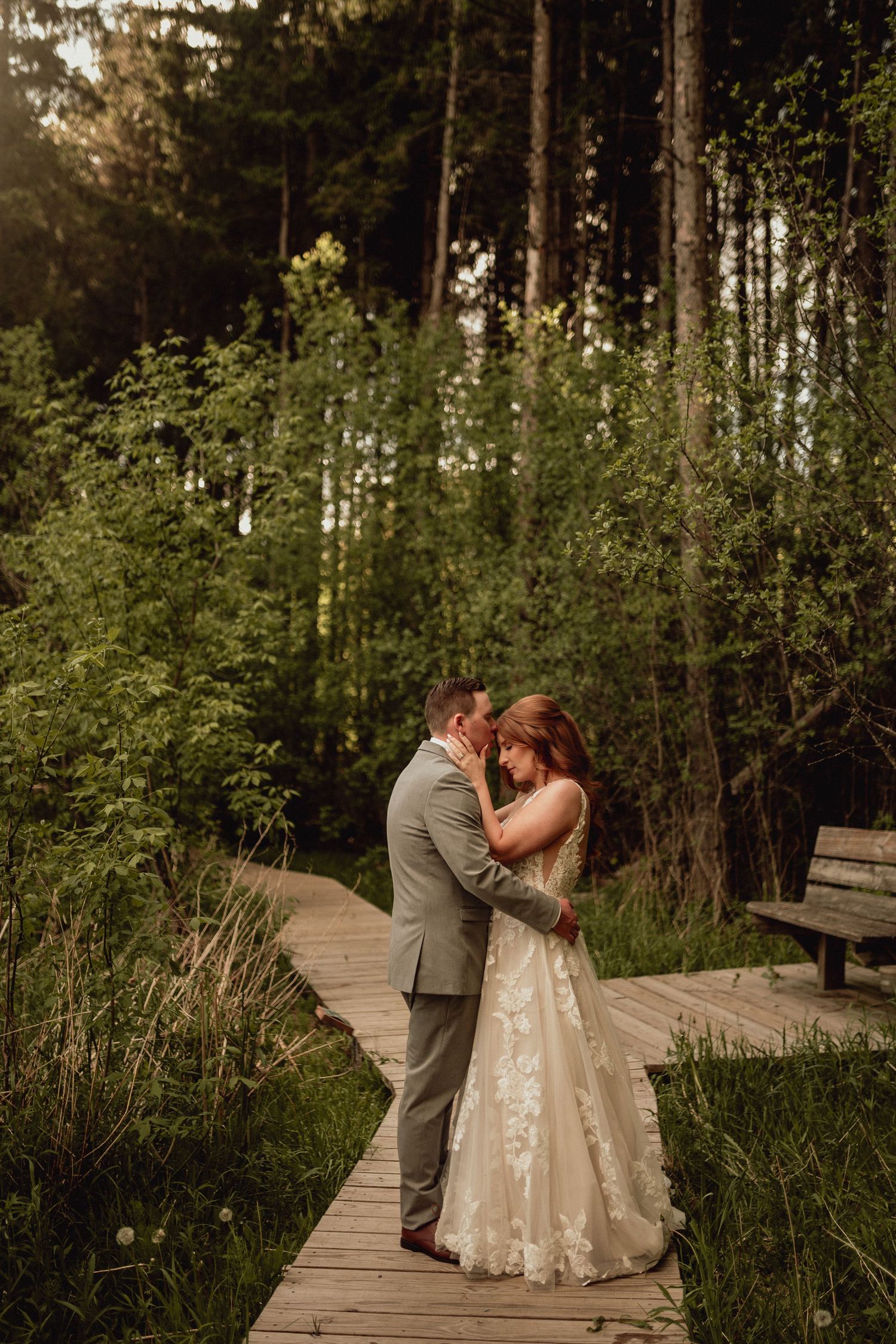 A couple shares an intimate moment on a wooden boardwalk surrounded by lush forest greenery.