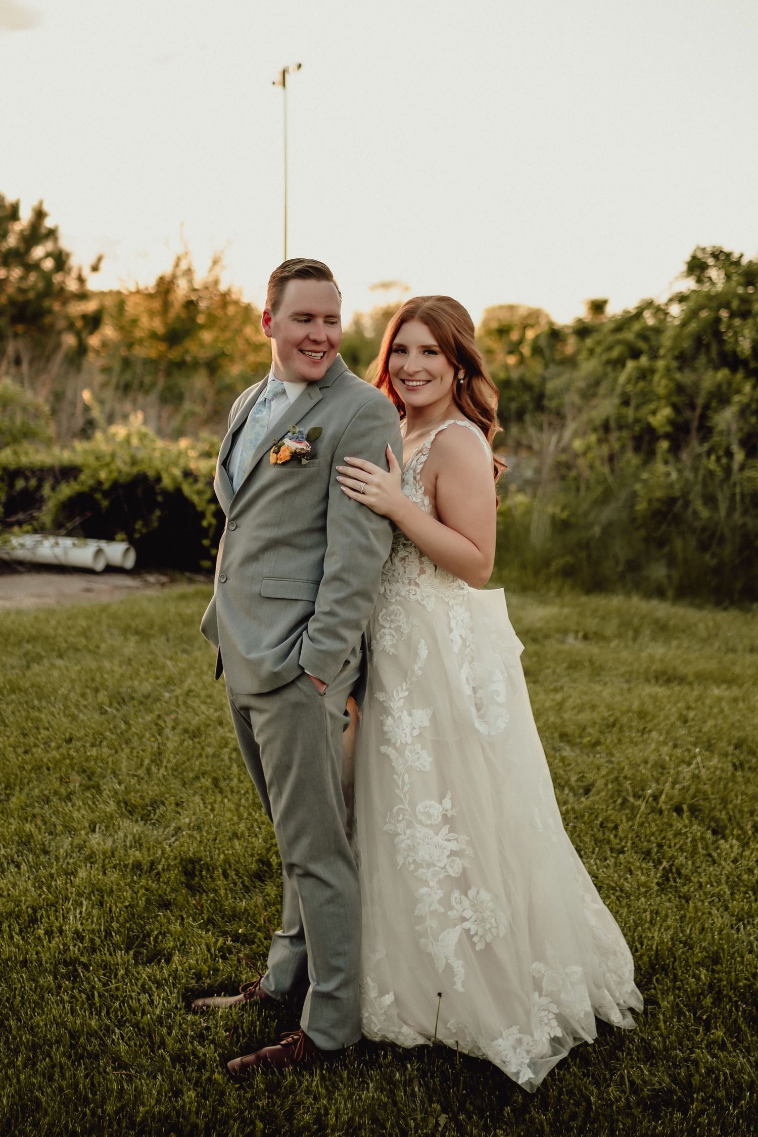 A happy wedding couple posing together in formal attire against a sunset backdrop.