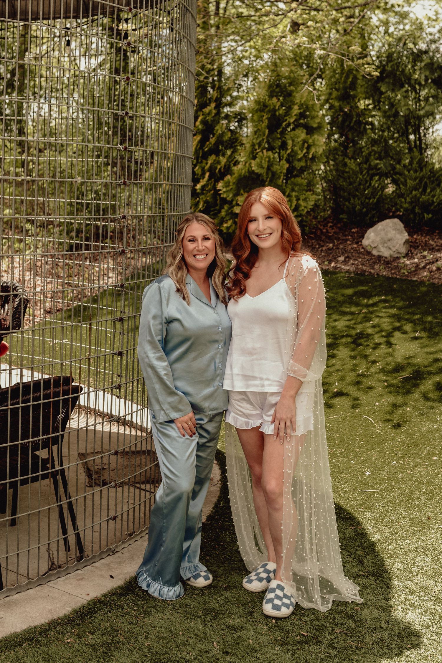 Two people pose together outdoors next to a decorative metal garden structure in a green backyard setting.