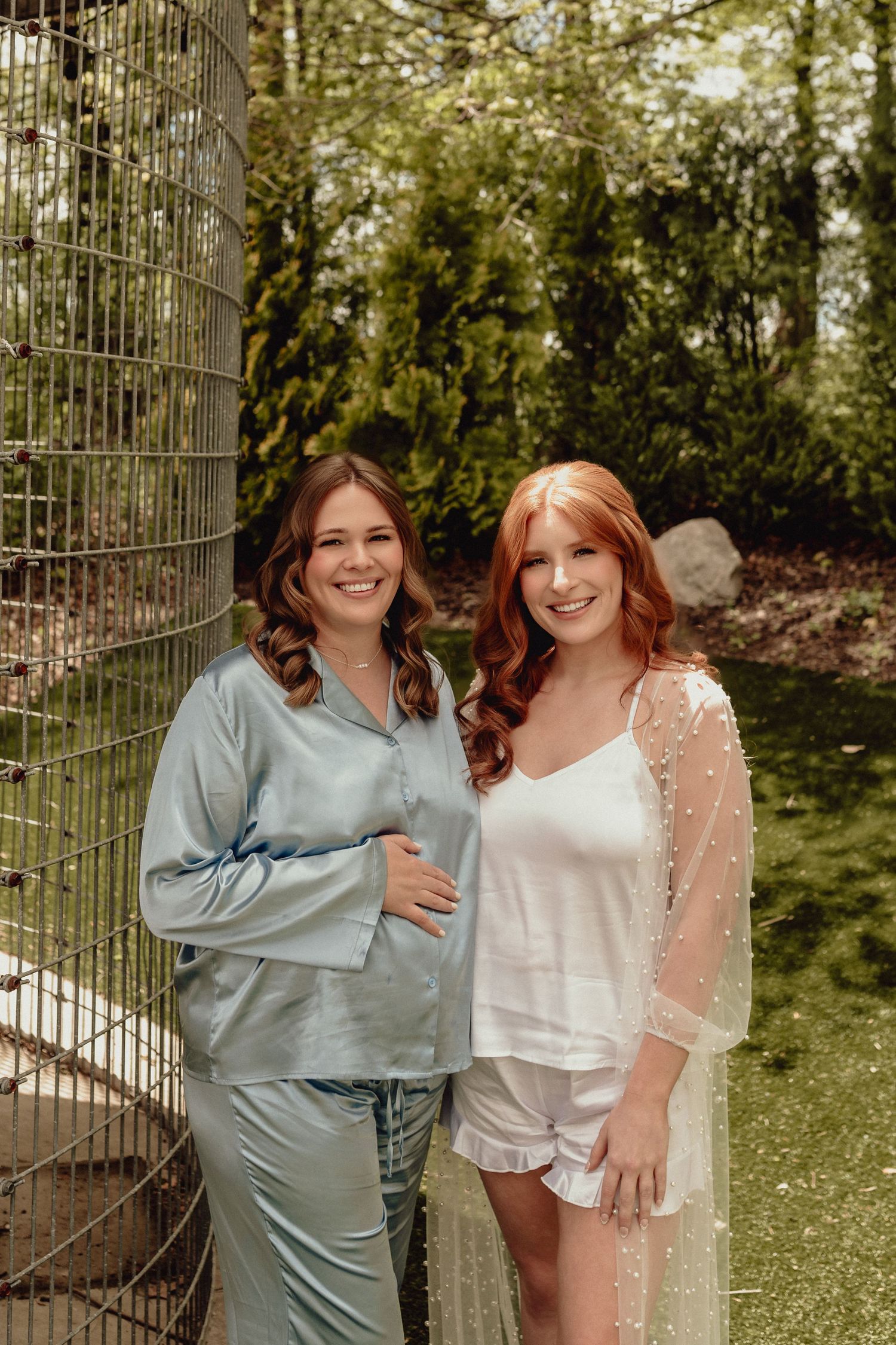 Two people in contrasting outfits, one in light blue silk and one in white lace, pose together in a garden setting.