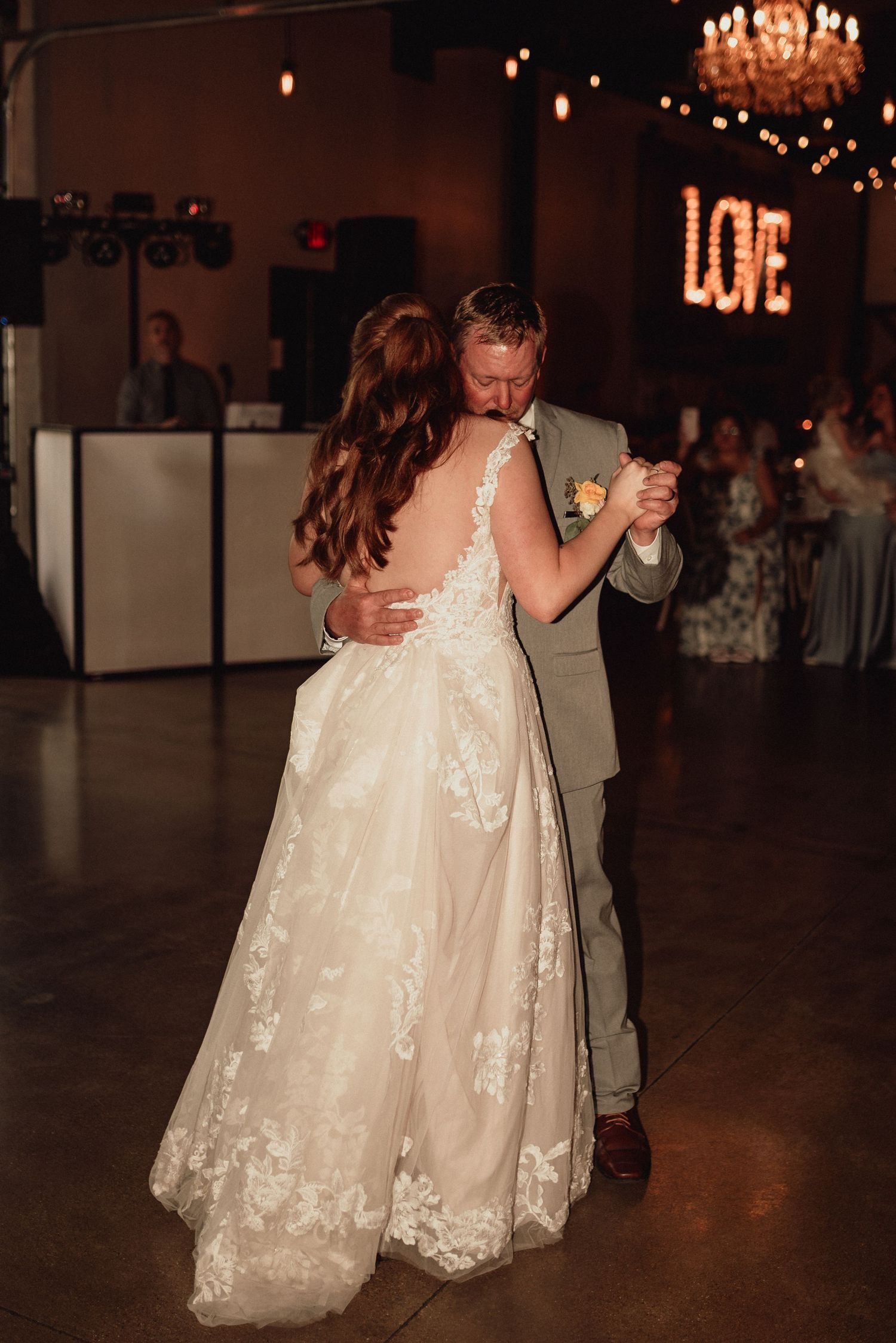 A couple shares a romantic dance at their wedding reception under warm chandelier lighting.