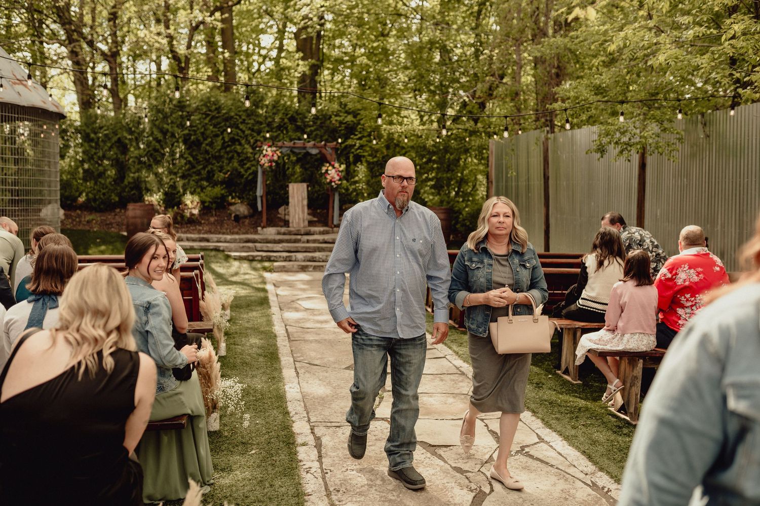 Wedding guests mingle and socialize during an outdoor garden reception at a daytime celebration.
