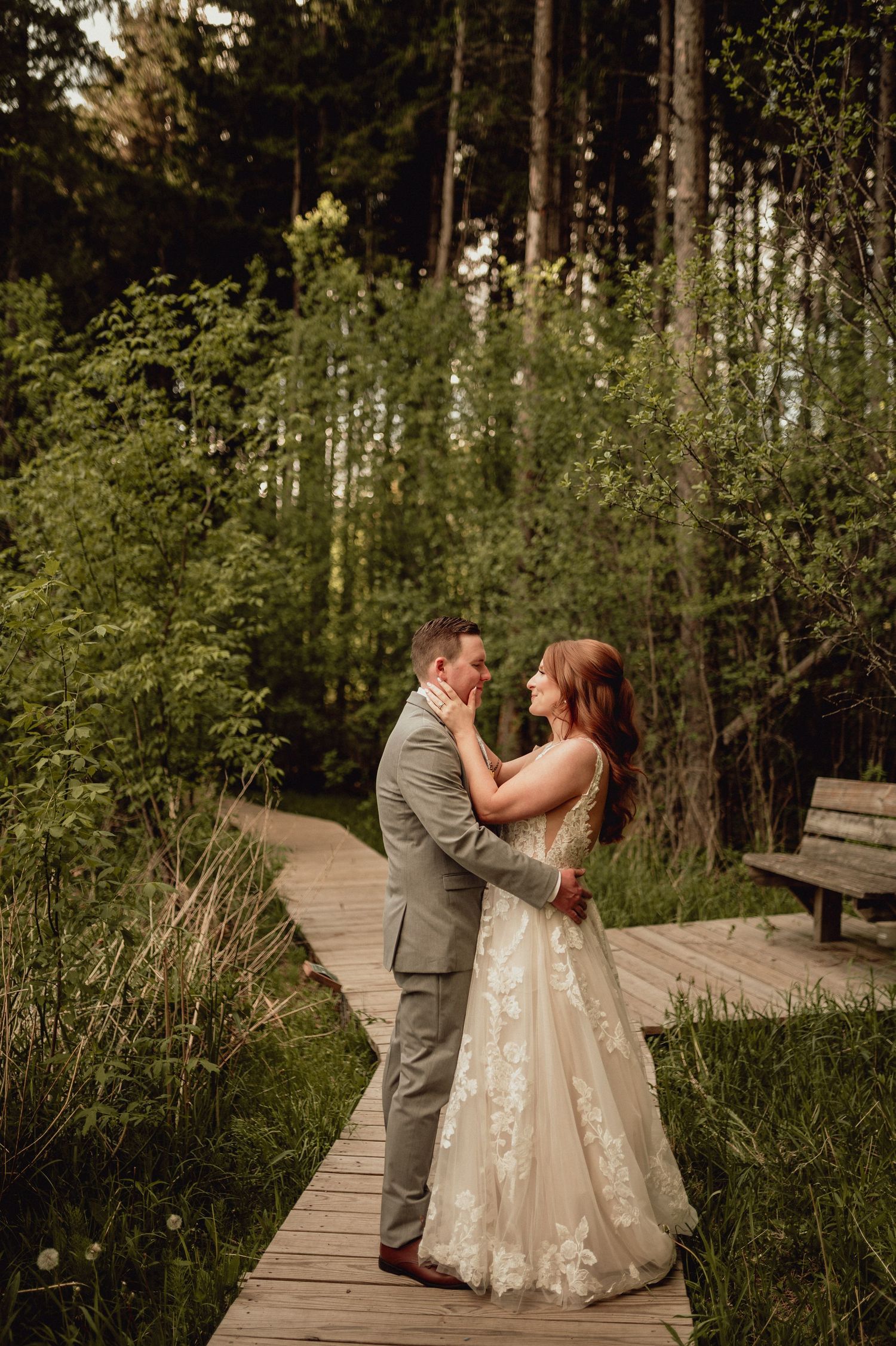 A couple shares romantic moments on a wooden boardwalk surrounded by lush greenery and trees.