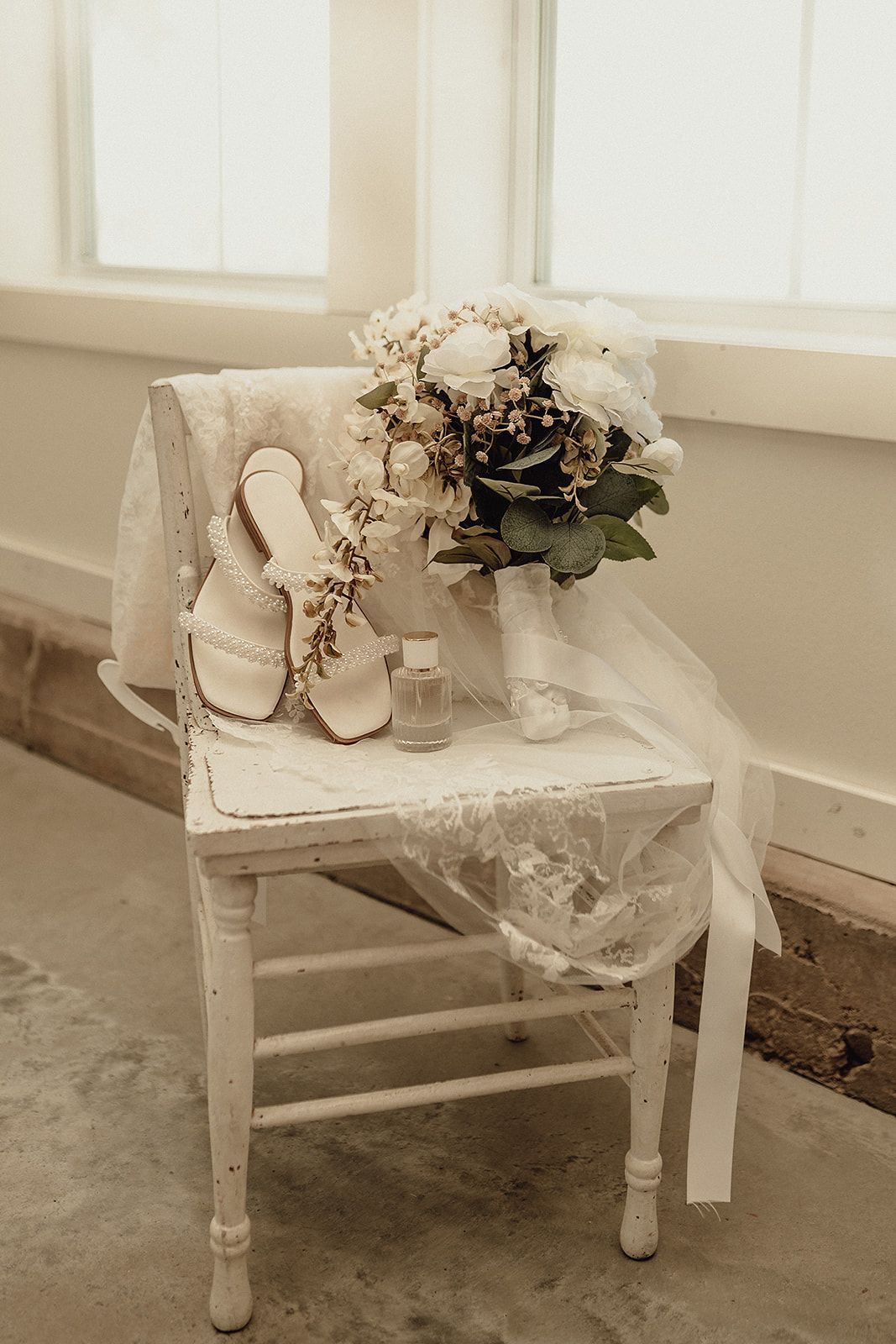 Rustic white bench displaying wedding shoes and delicate floral arrangements.