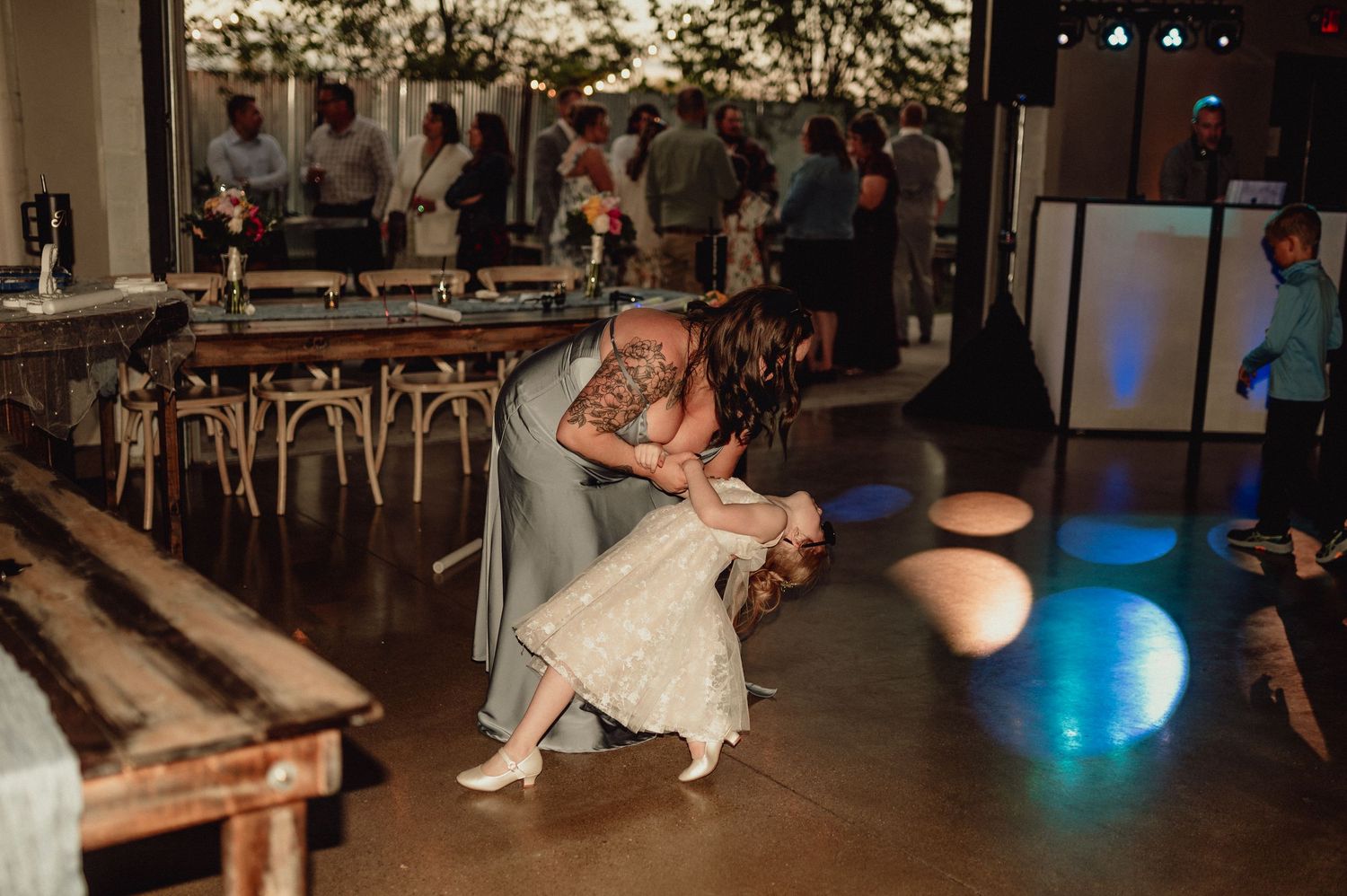 People dancing and celebrating at a dimly lit wedding reception venue with blue accent lighting.