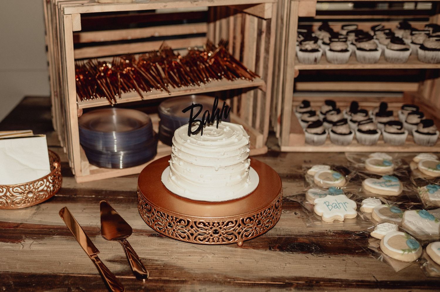Rustic dessert display featuring a white wedding cake and chocolate covered treats on wooden crates.