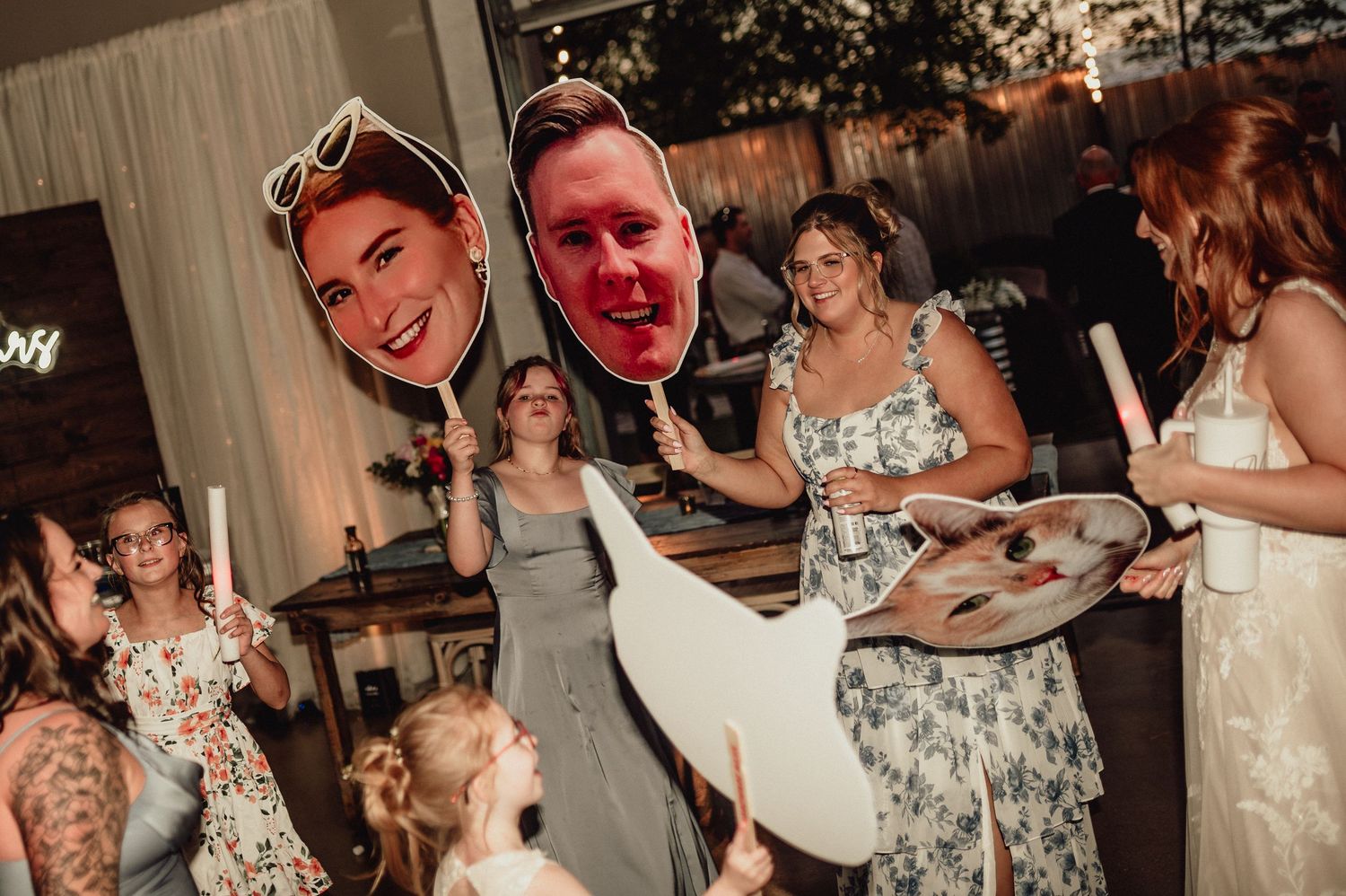 Wedding guests dancing and celebrating on a dance floor at a reception venue with festive lighting and decor.
