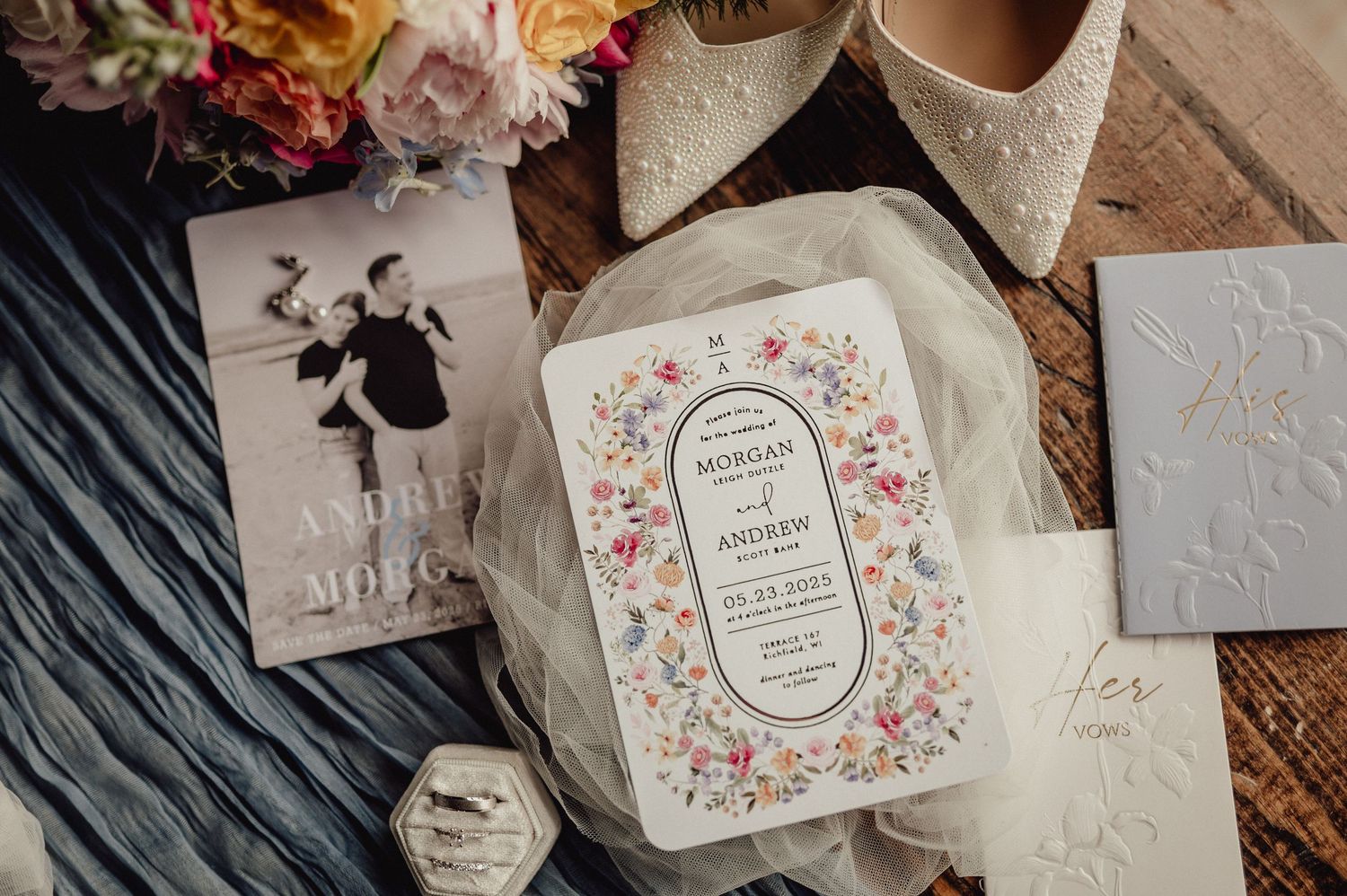 Elegant wedding invitation suite with floral designs and calligraphy laid out on a rustic wooden surface.