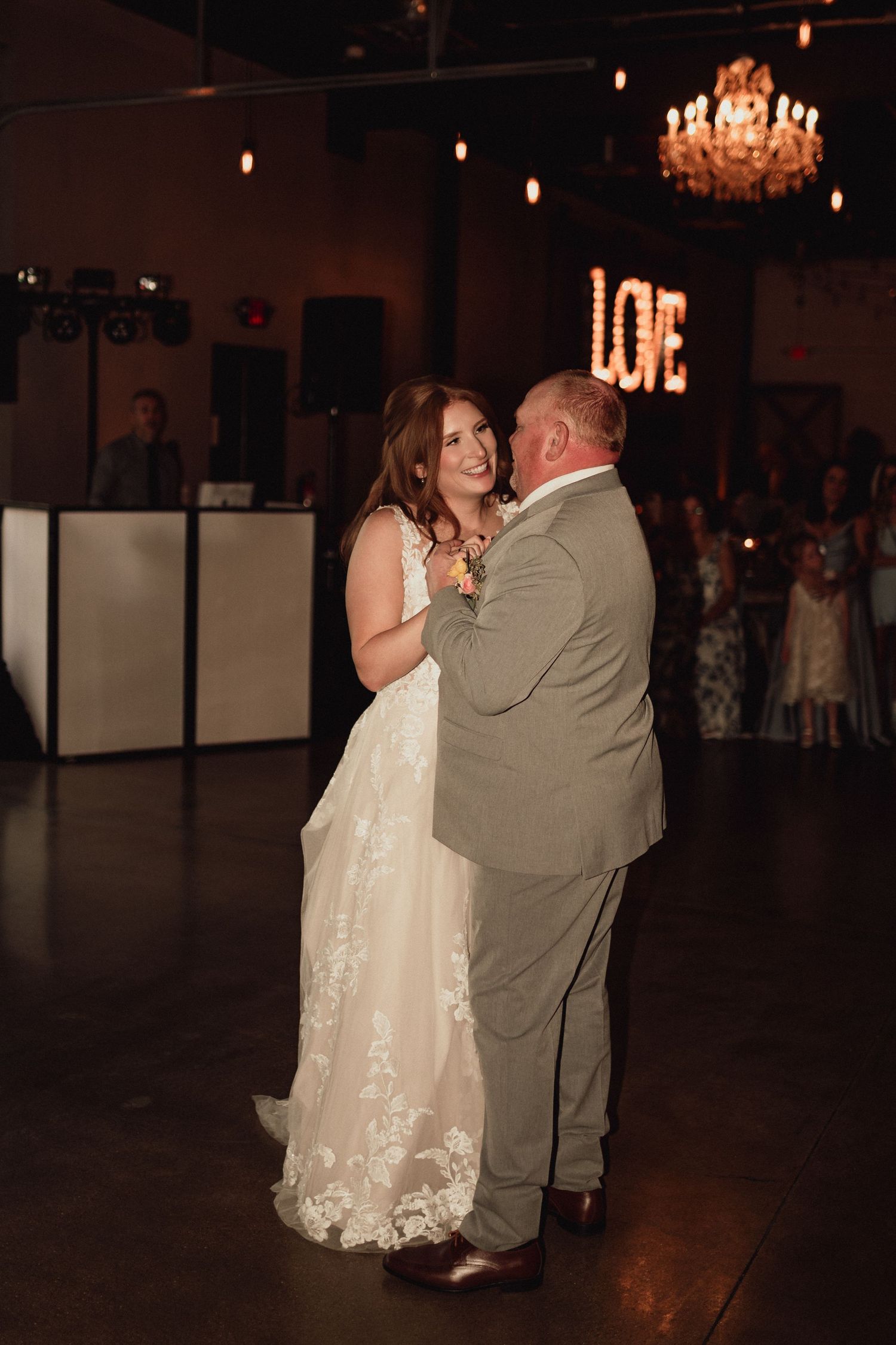A couple shares a romantic dance at their wedding reception under warm lighting and chandeliers.