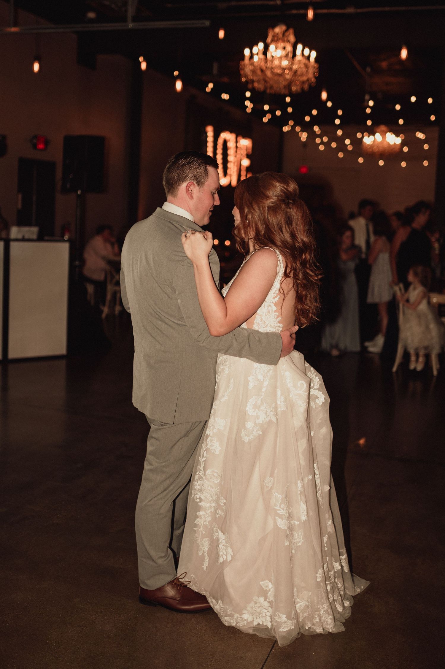 A couple dances together at a wedding reception under warm lighting and a chandelier.