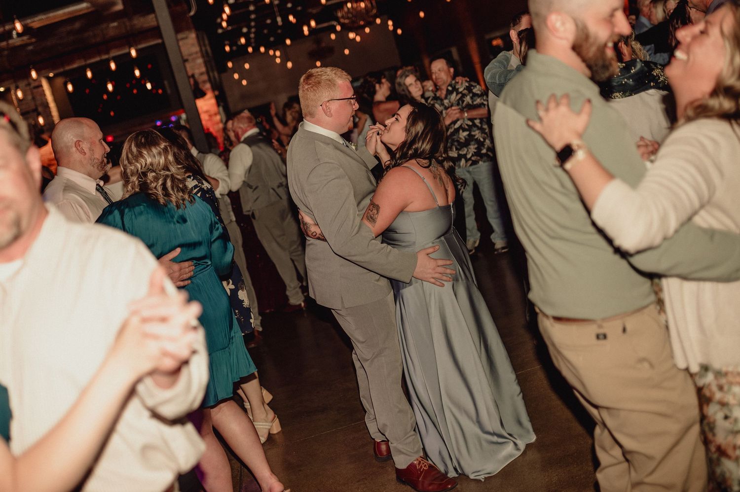 A crowd of people dancing and celebrating at a lively party with twinkling lights in the background.