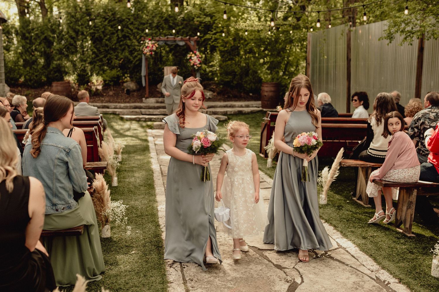 Wedding guests dance and celebrate outdoors in a garden setting during a festive summer reception party.