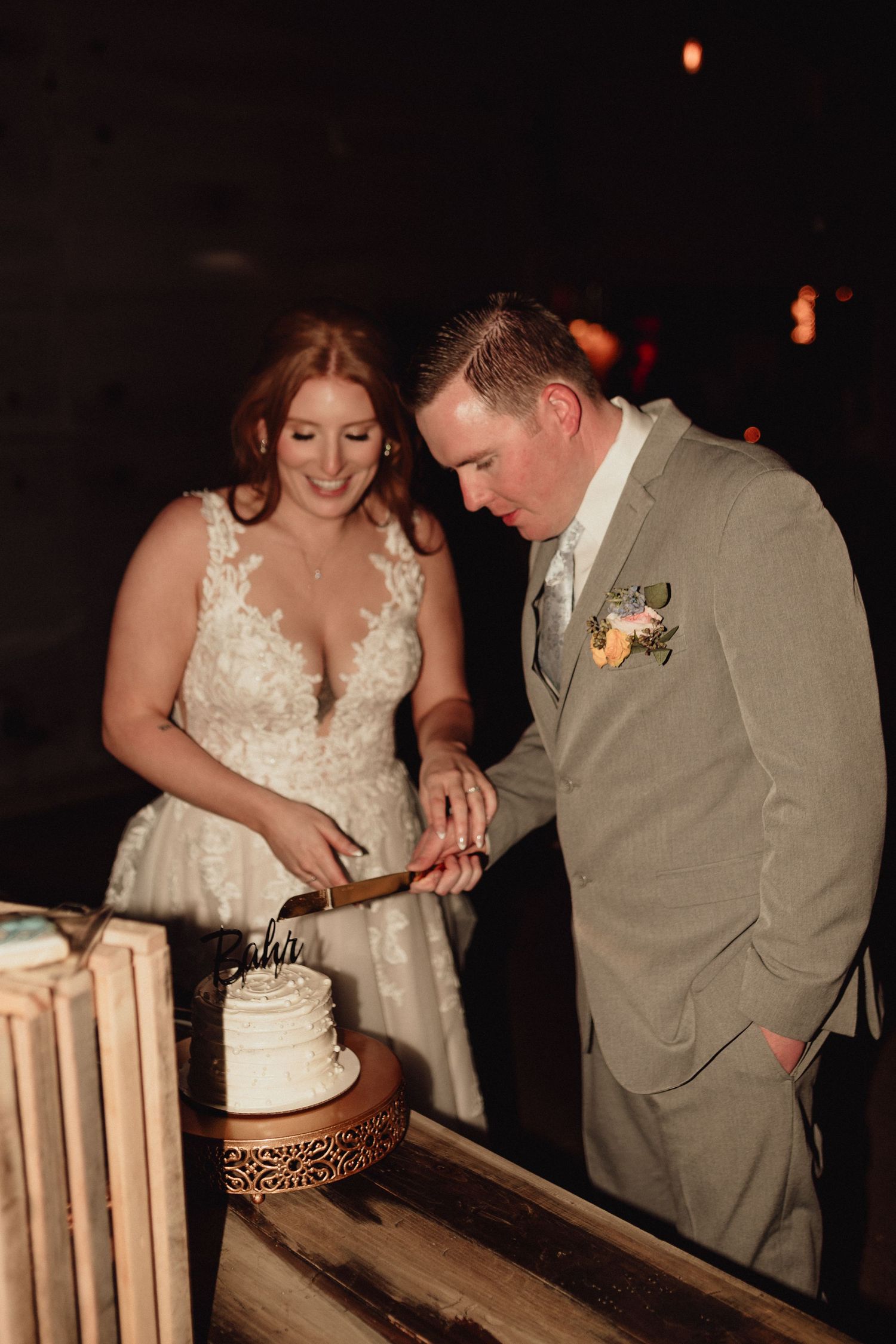 Newlyweds participate in a traditional wedding cake cutting ceremony at their reception in a dimly lit venue.