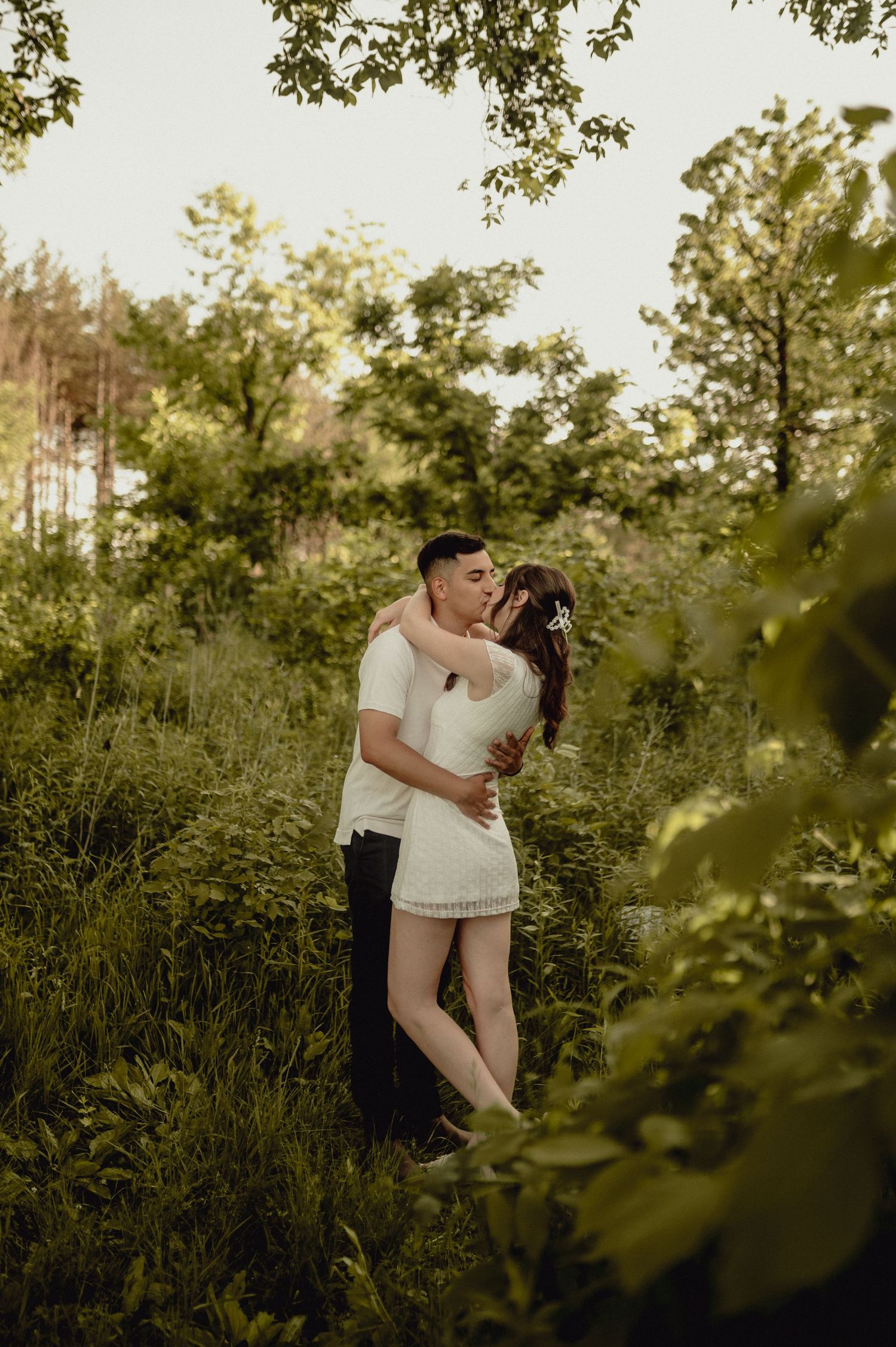 A romantic embrace in a lush green natural setting during golden hour.