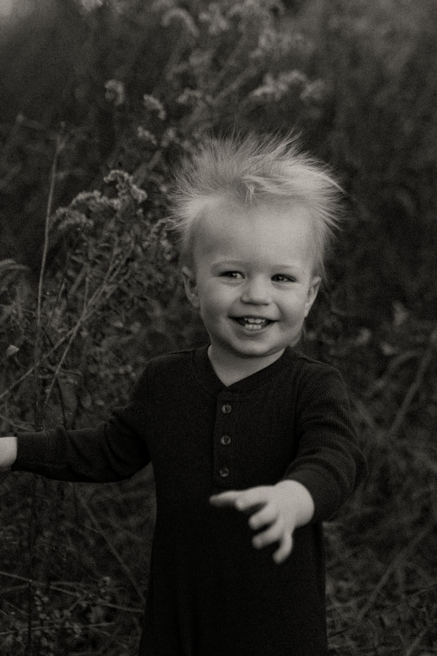 Black and white portrait of joyful toddler with spiky hair outdoors.