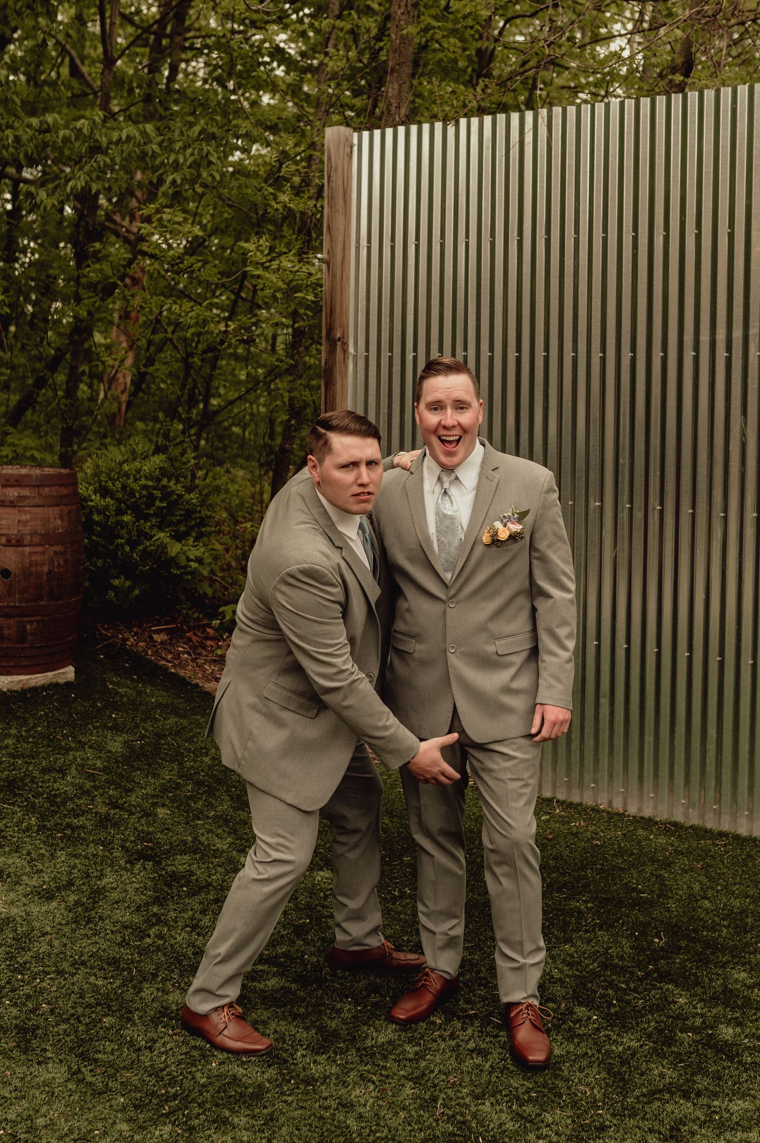 Two people in matching gray suits pose playfully in a sequence of four photos on grass with a fence in background.