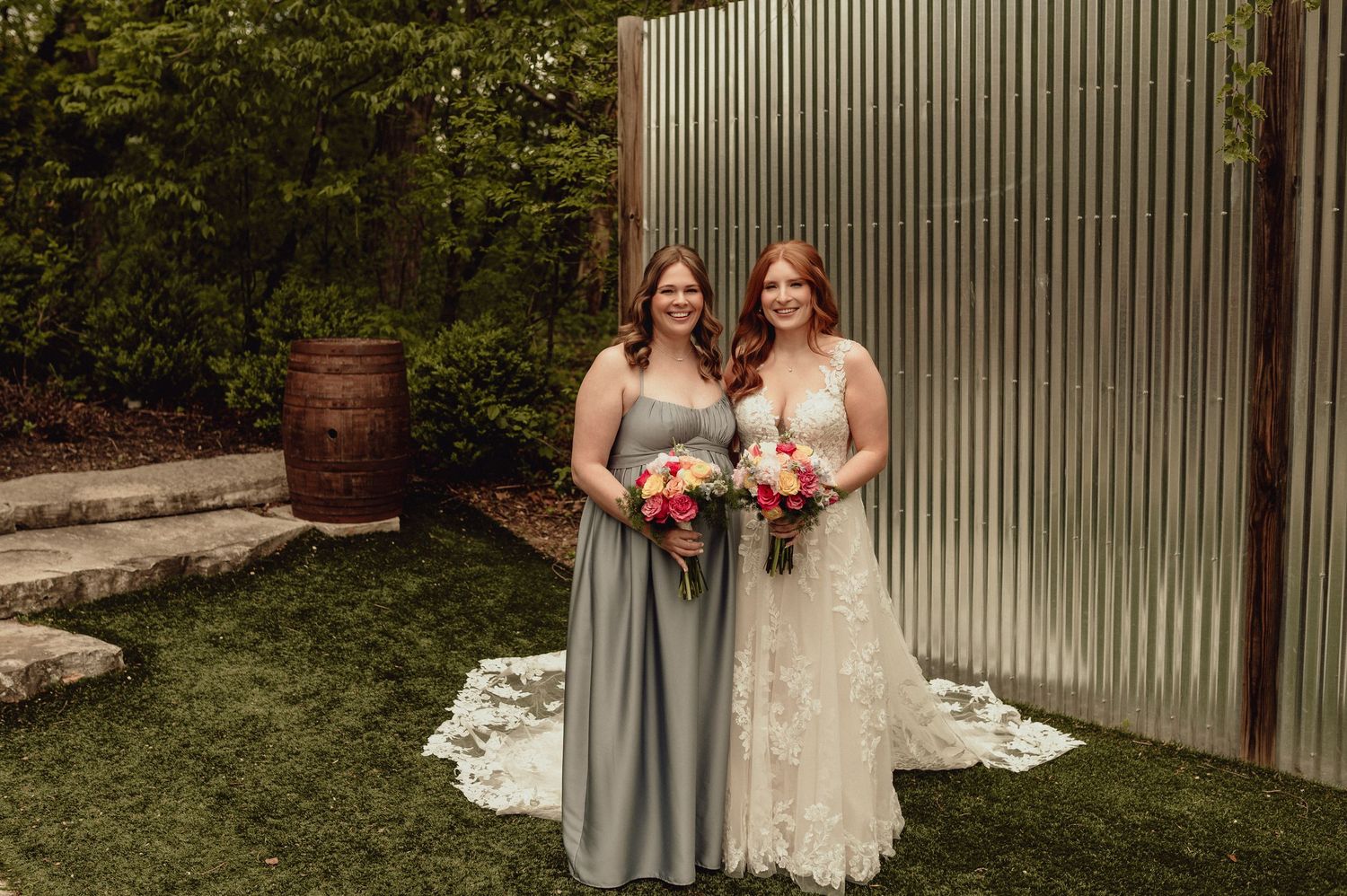 Wedding party poses together in front of a gray corrugated wall in an outdoor garden setting.