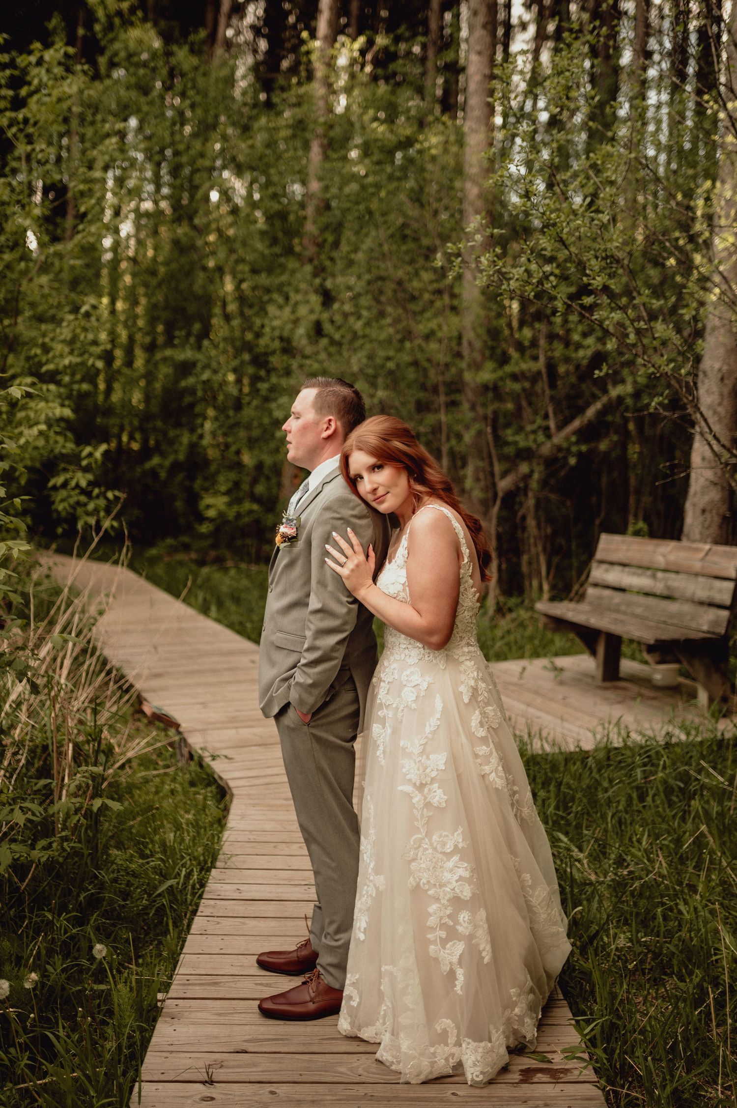 A couple shares their first look moment on a wooden boardwalk surrounded by lush forest greenery.