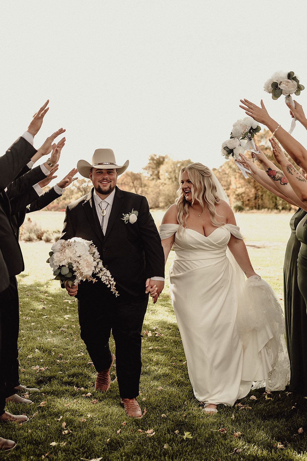 Wedding party celebrates on grass with raised hands and joyful movements.