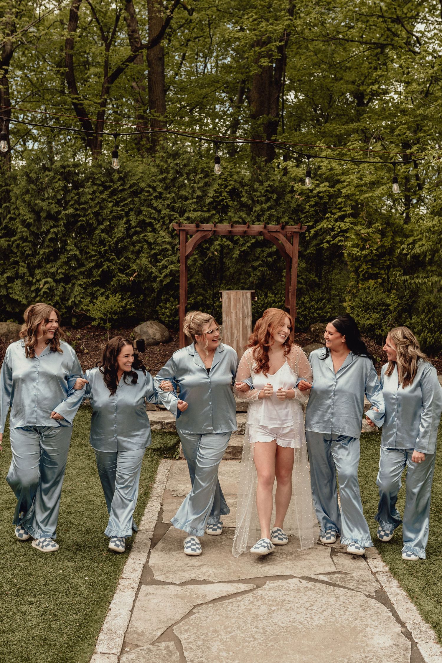 A group in matching blue pajamas walks together on a garden path while laughing and having fun.