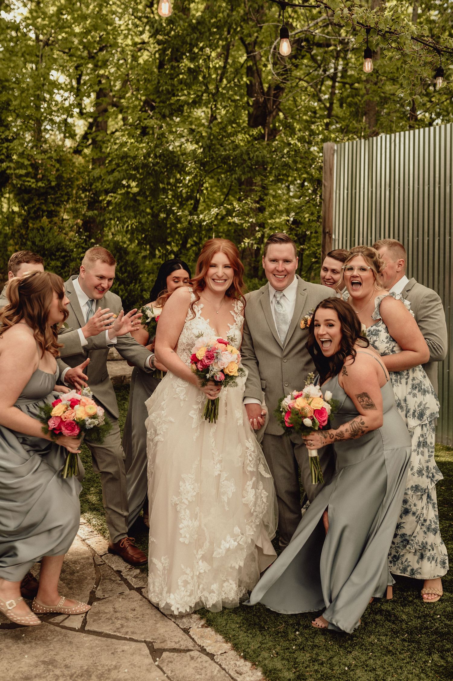 Candid moment of wedding party sharing laughter during outdoor photo session in gray attire.