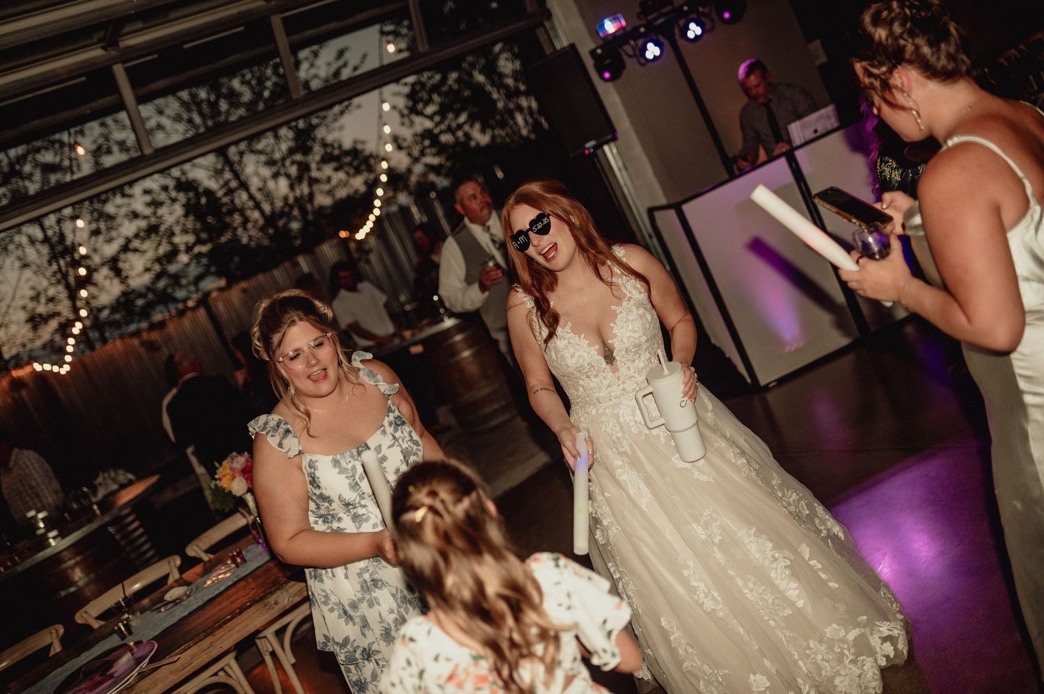 People dancing and celebrating at a wedding reception with purple lighting and festive atmosphere.