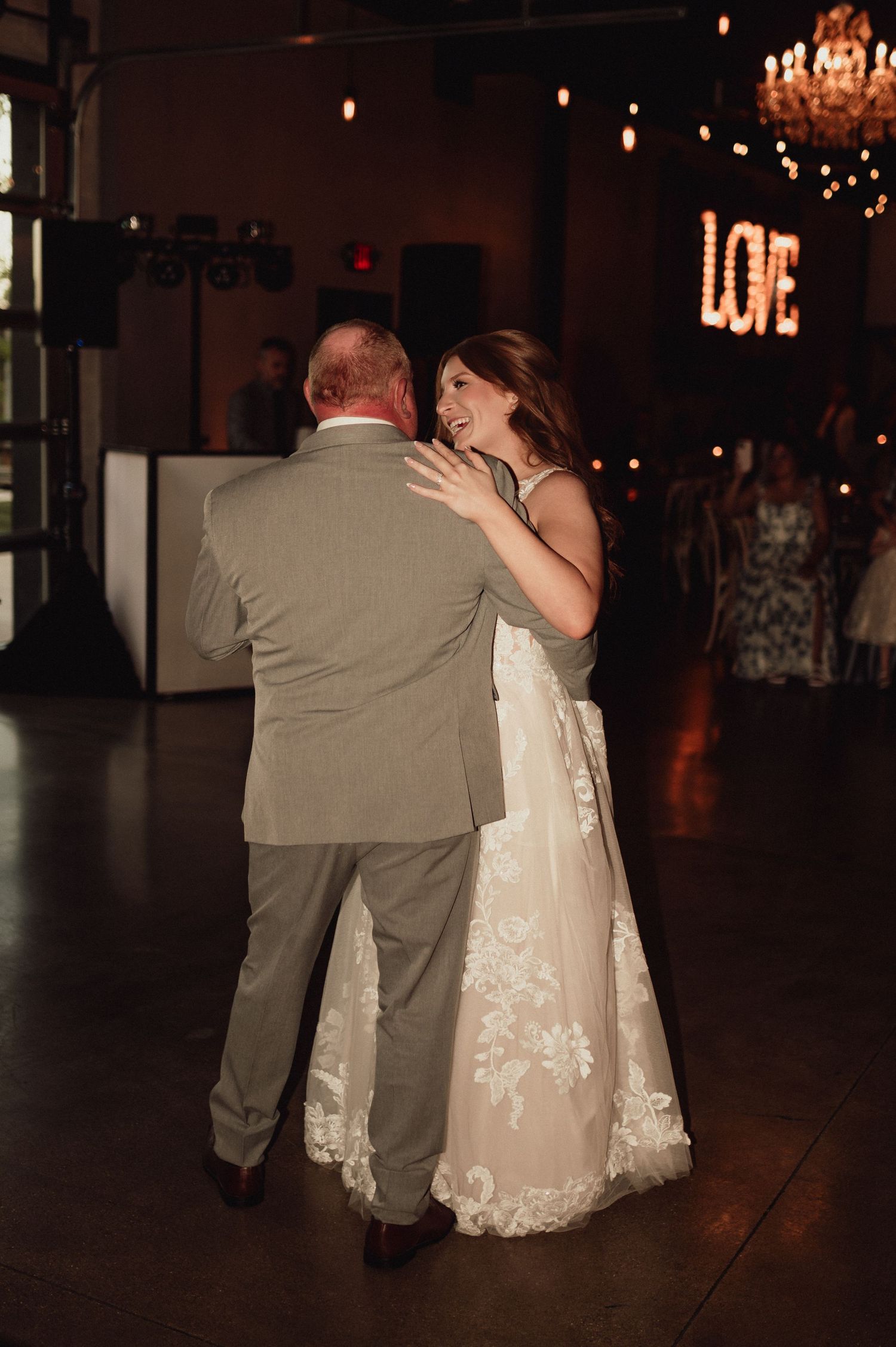 A couple shares an intimate dance at their wedding reception with a glowing LOVE sign in the background.