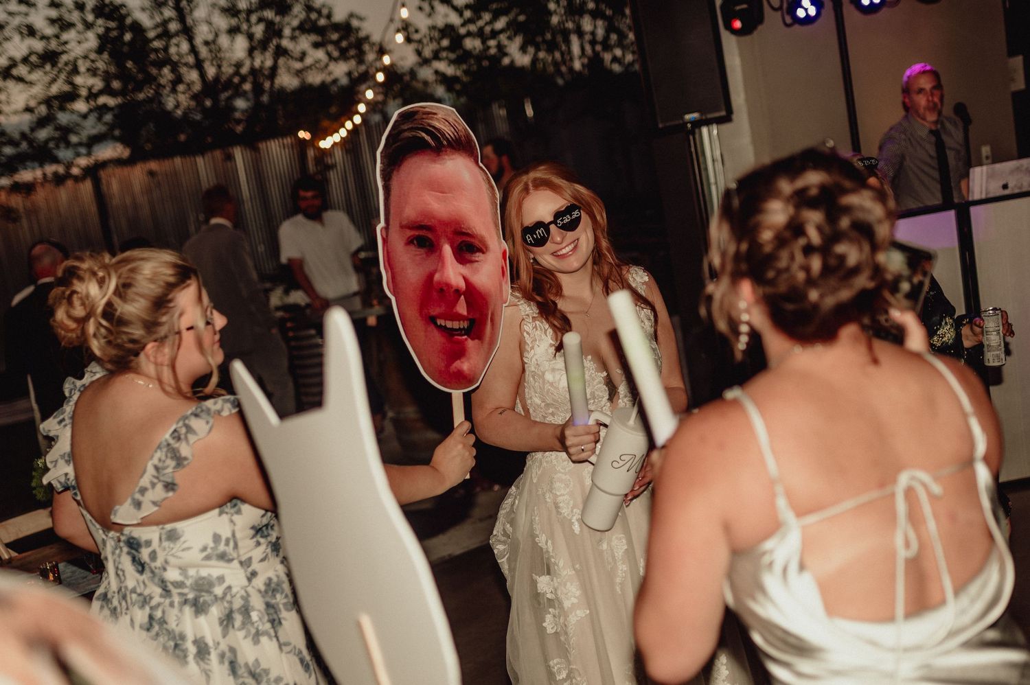 People dancing and laughing at a wedding reception with string lights glowing in the background.