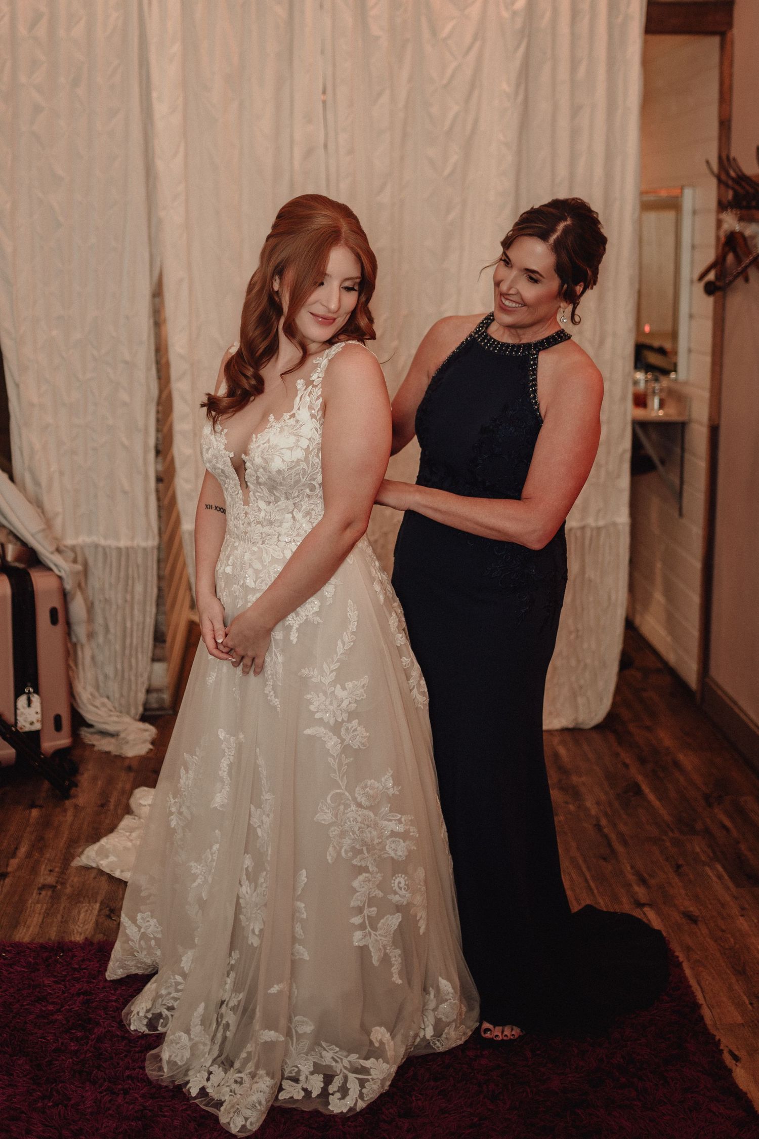 Two people share an intimate moment in a room with wooden floors and curtains while one wears a flowing white dress.