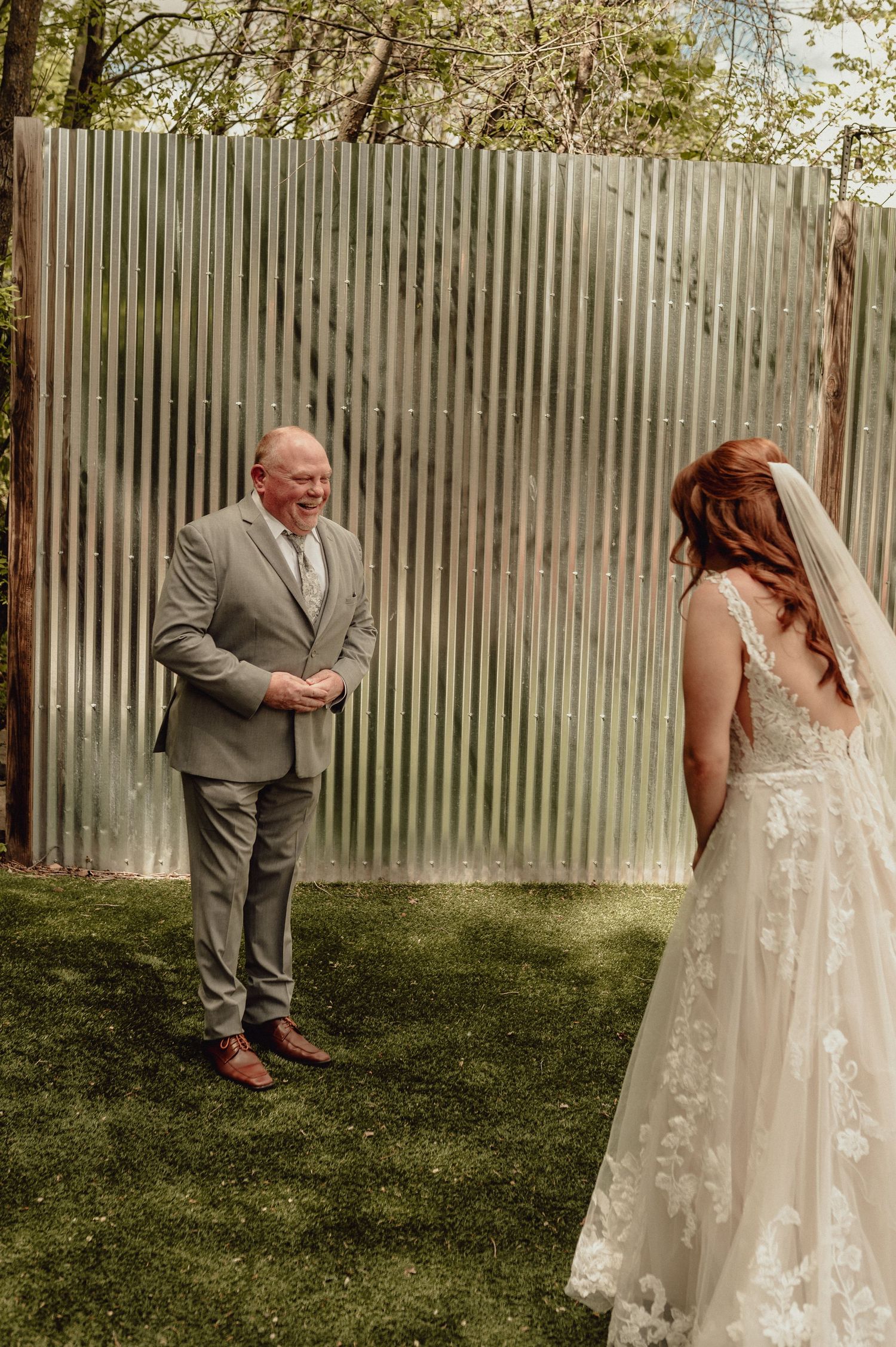 A wedding couple shares a sweet first look moment in a backyard garden setting with a wooden fence backdrop.