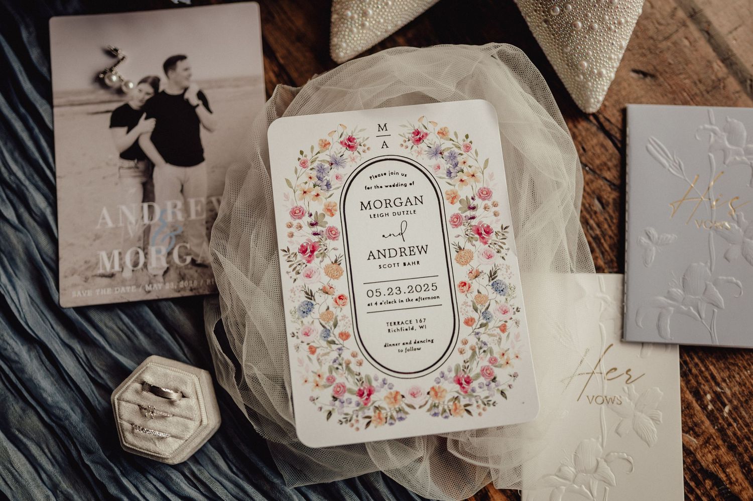 Elegant wedding invitation suite with floral designs and calligraphy displayed on rustic wooden background.