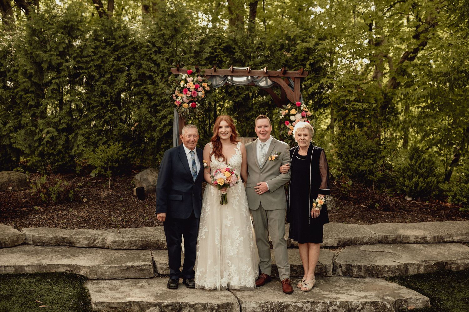 A wedding party poses together in a lush garden setting during an outdoor ceremony.