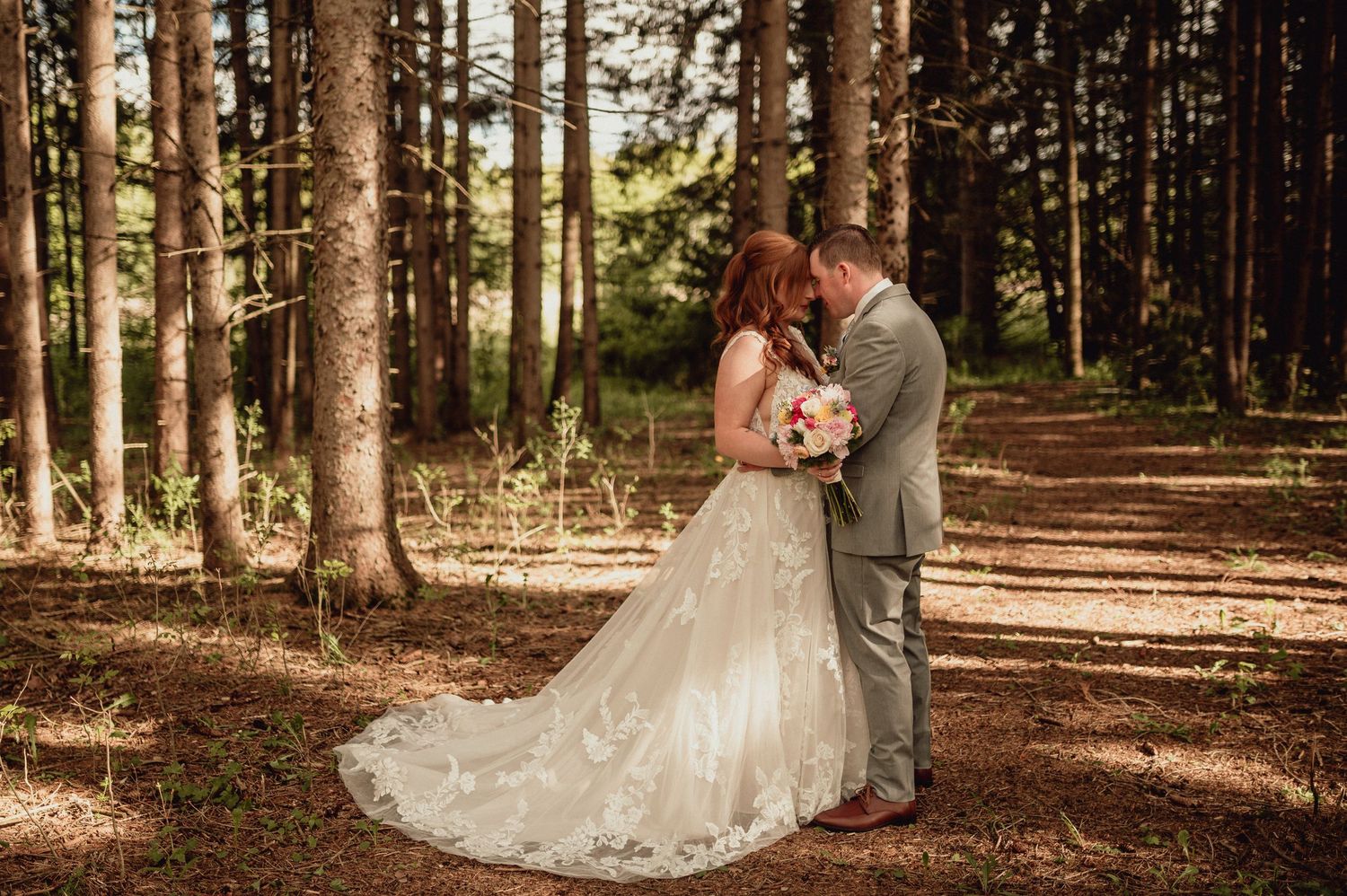 A romantic forest wedding photoshoot with sunlight streaming through tall evergreen trees in the background.