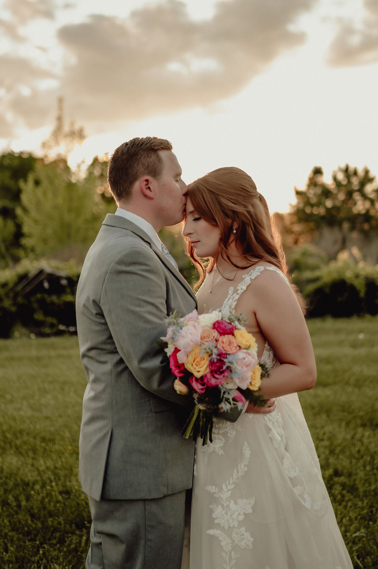 A couple shares an intimate moment at sunset during their outdoor wedding ceremony with a colorful bouquet.