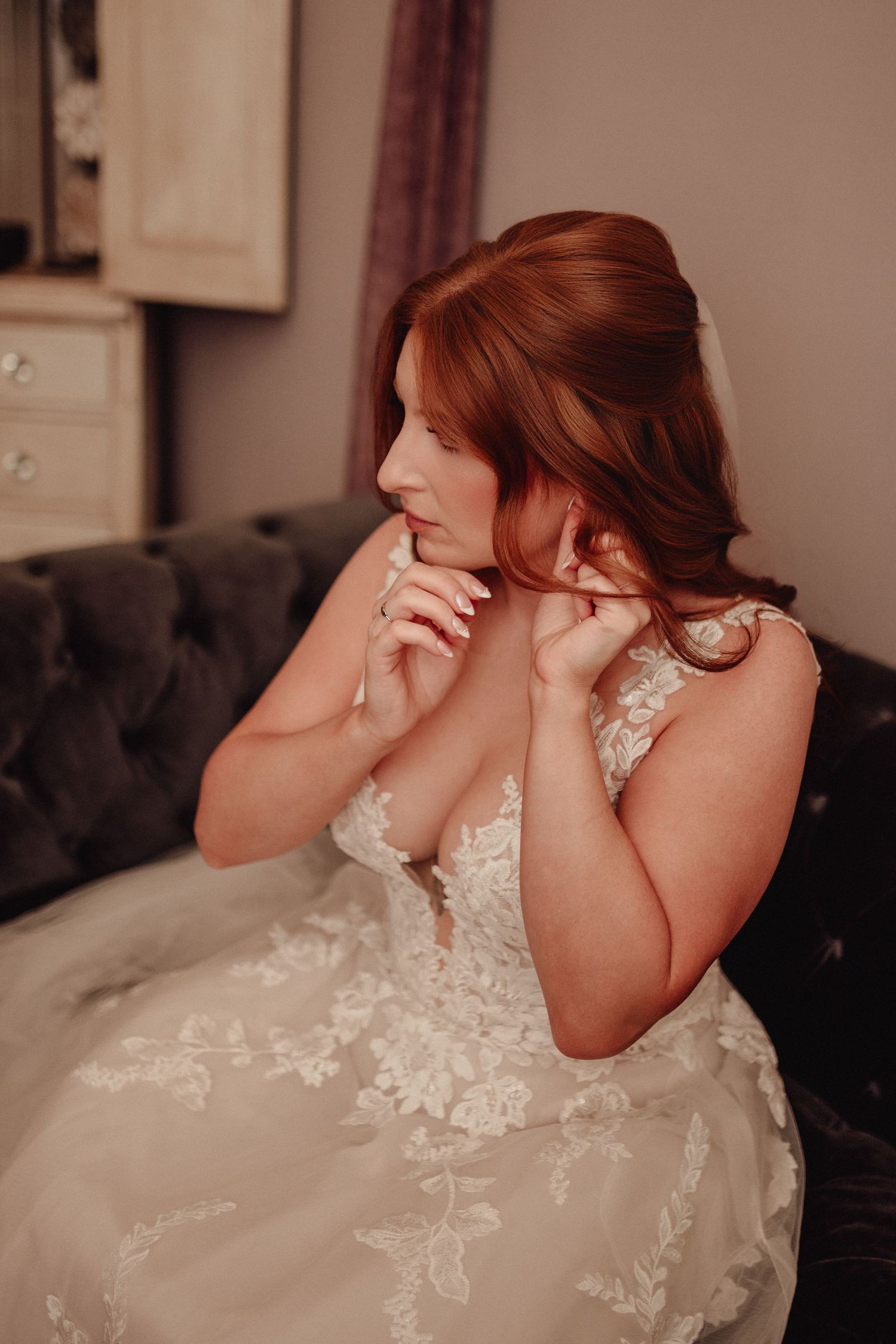 Emotional bride in lace wedding dress covers her face with her hands in a candid moment.