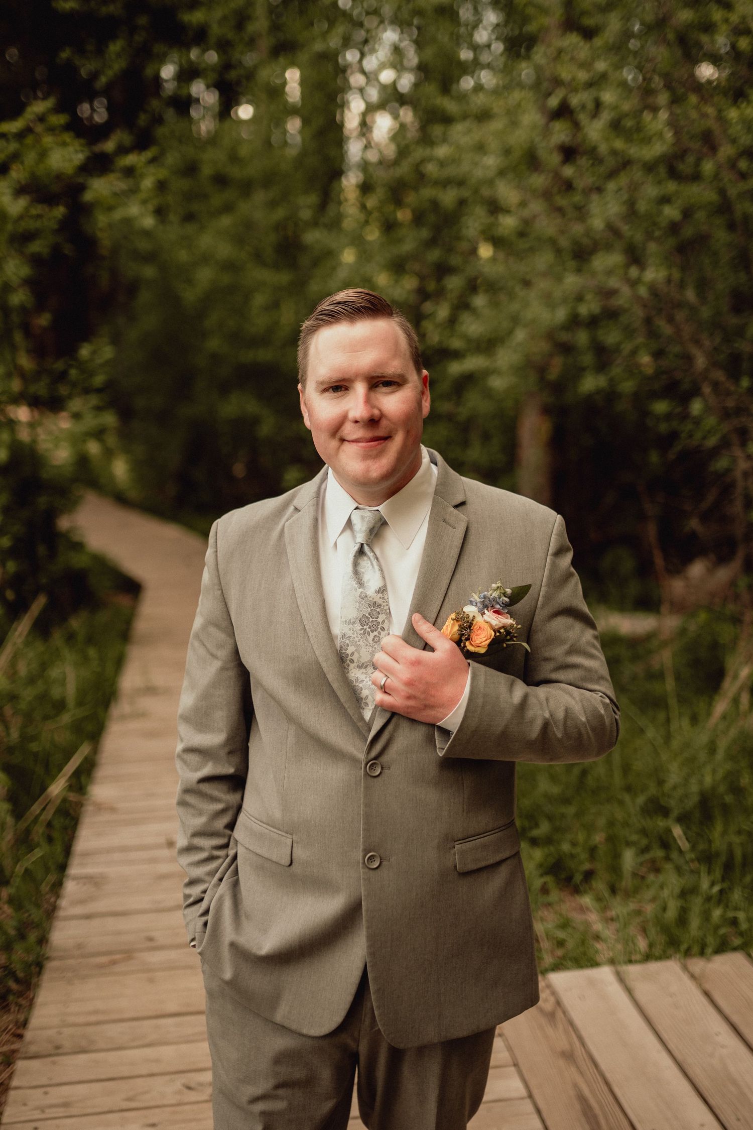 A person in a tan suit and tie poses on a wooden boardwalk surrounded by green foliage in a series of shots.
