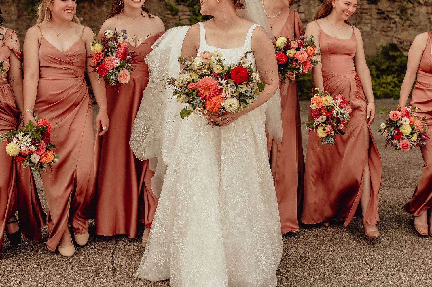 Wedding party photo showing bridesmaids in coral dresses with floral bouquets.