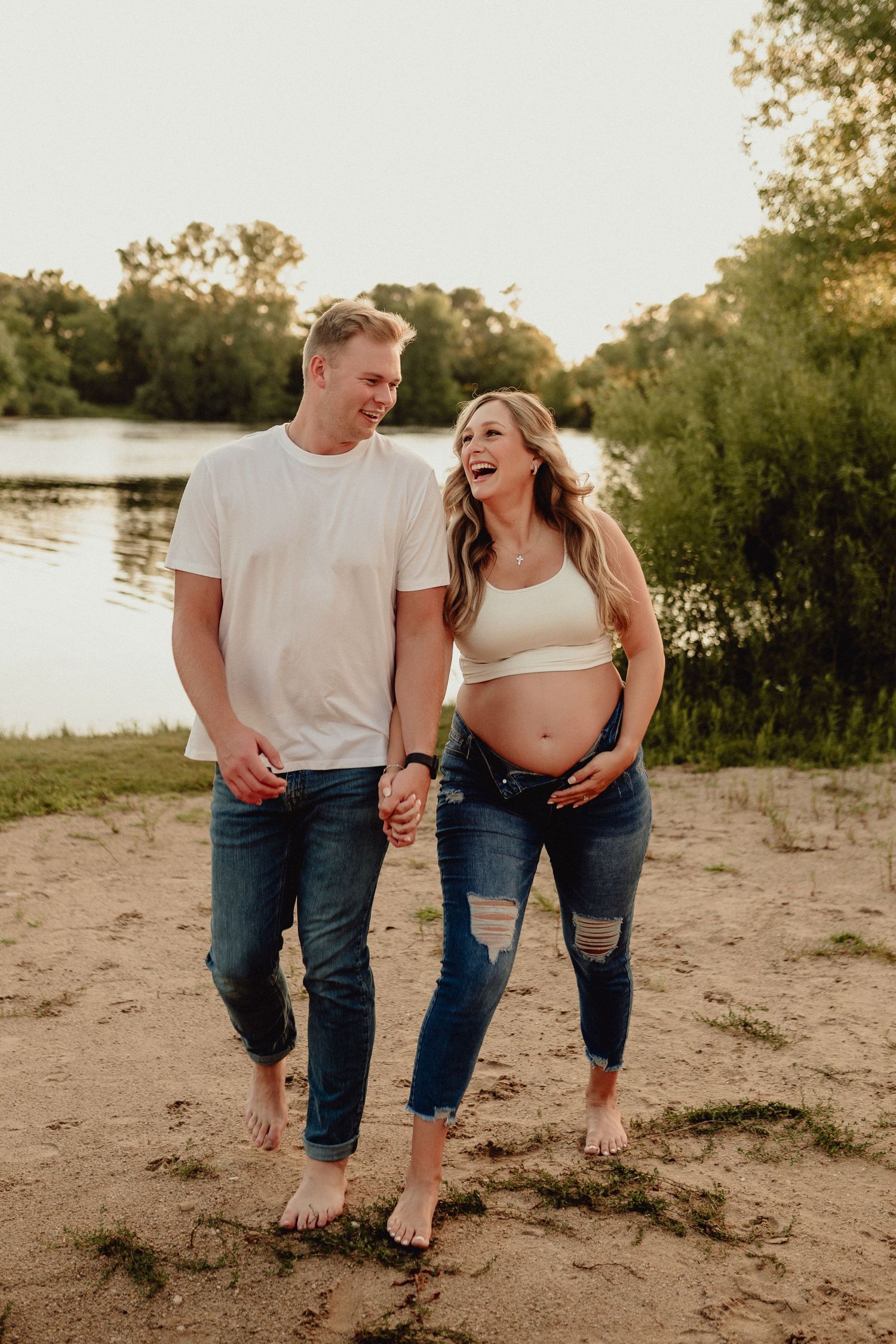 Candid outdoor photo of couple laughing together on sandy beach at sunset.