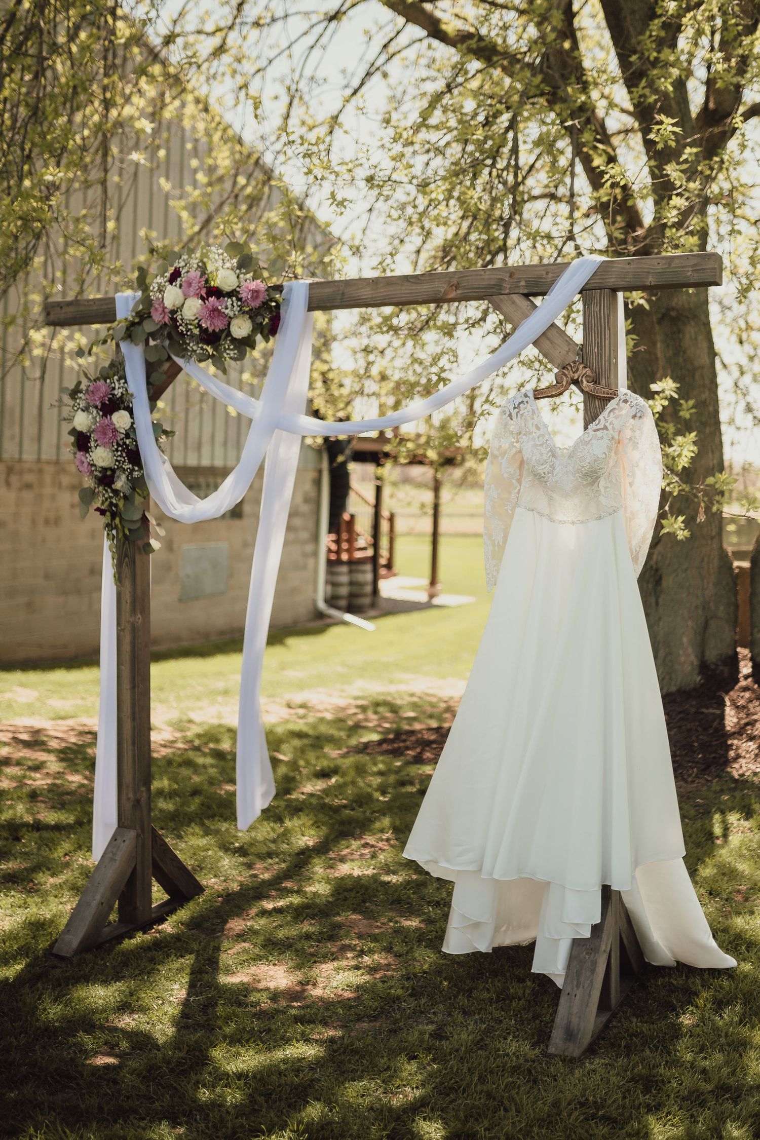 White wedding dresses hanging on wooden cross display outdoors with floral decorations.
