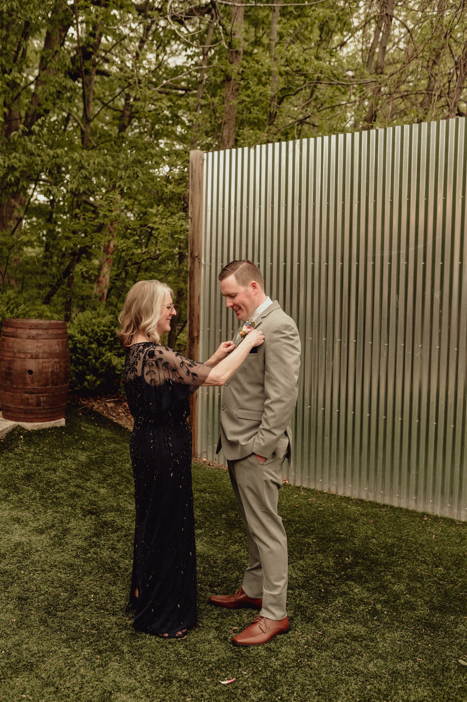 A couple shares a romantic moment in front of a corrugated metal wall and greenery during an outdoor photoshoot.