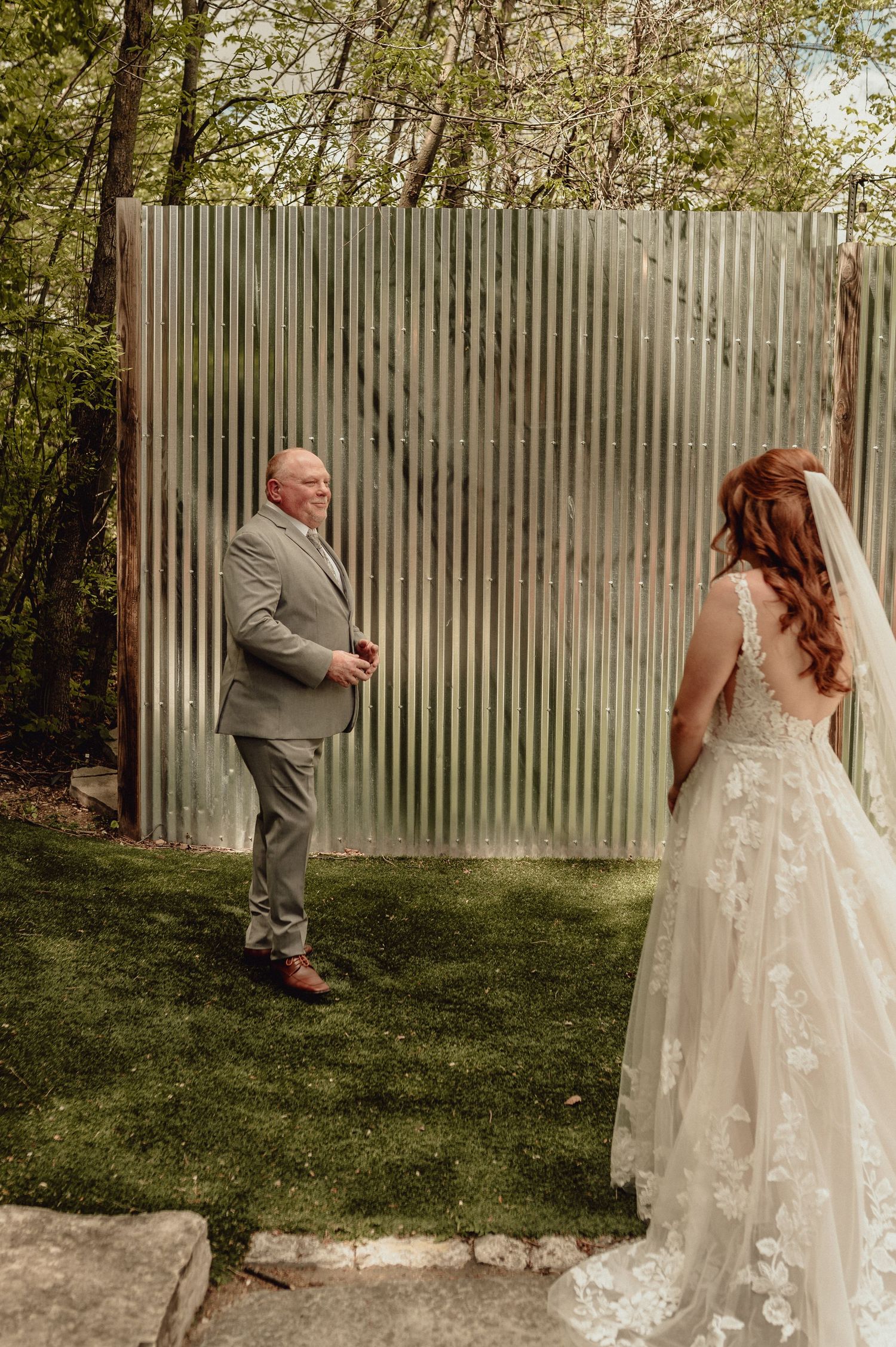 A couple poses for wedding photos in front of a rustic wooden fence surrounded by greenery.