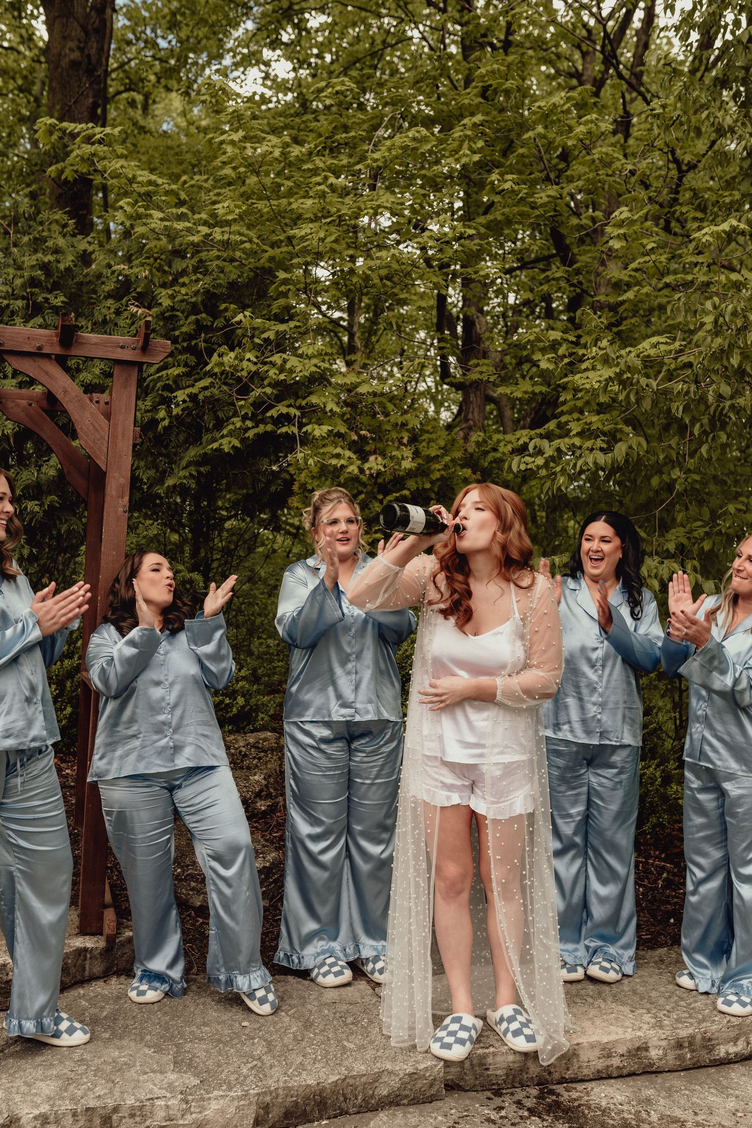 Wedding party in coordinated grey outfits celebrates joyfully on stone wall.
