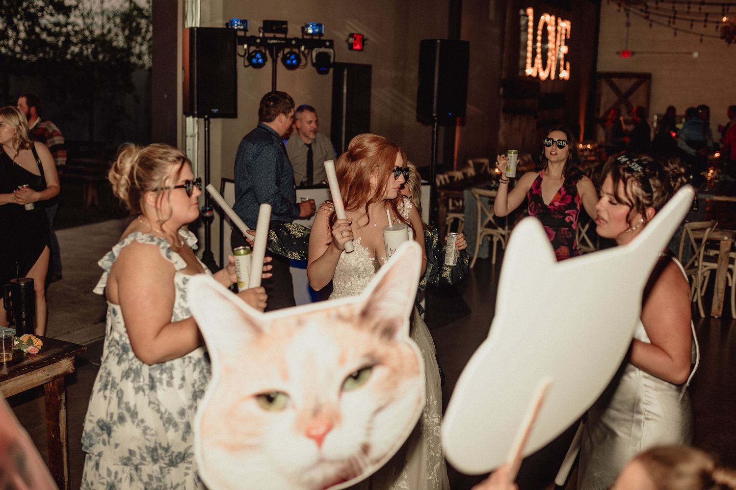 Wedding reception guests dance and celebrate on a crowded dance floor in an indoor venue with dim lighting.