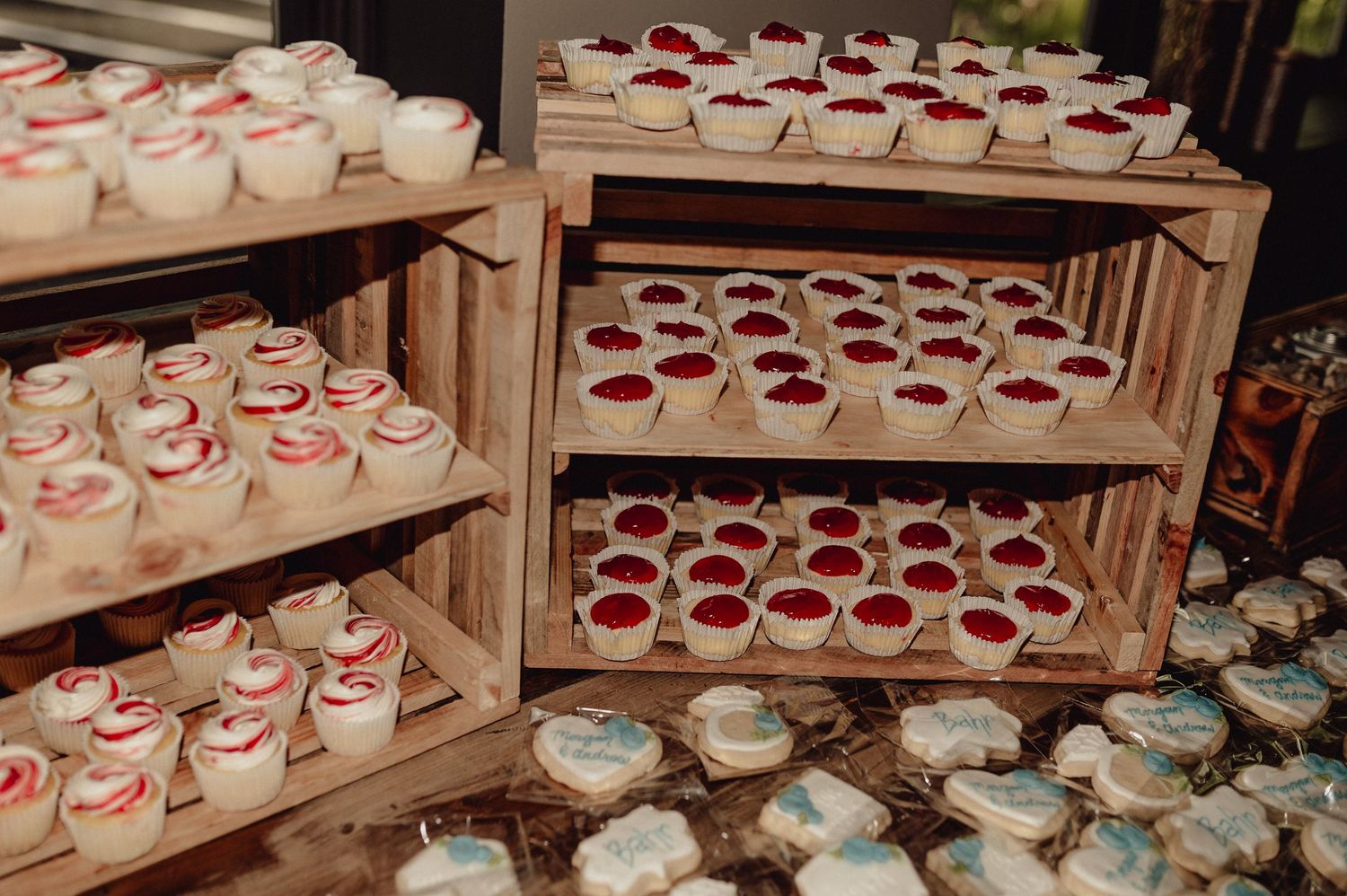 Rows of white dessert cups with red garnishes are arranged on wooden display shelves at a catering event.