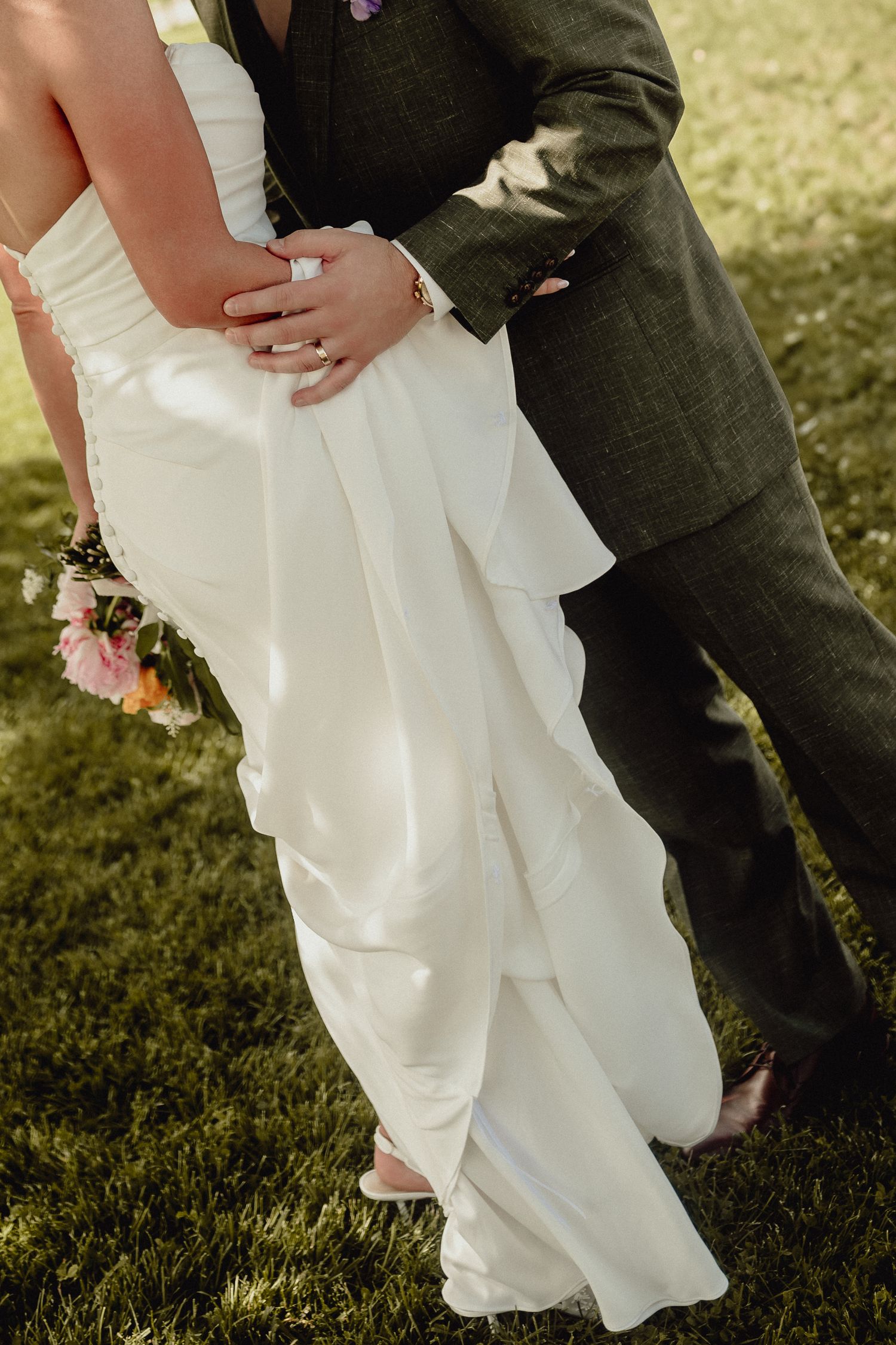 Close-up wedding photo of couple embracing outdoors, focusing on white dress details and suit.