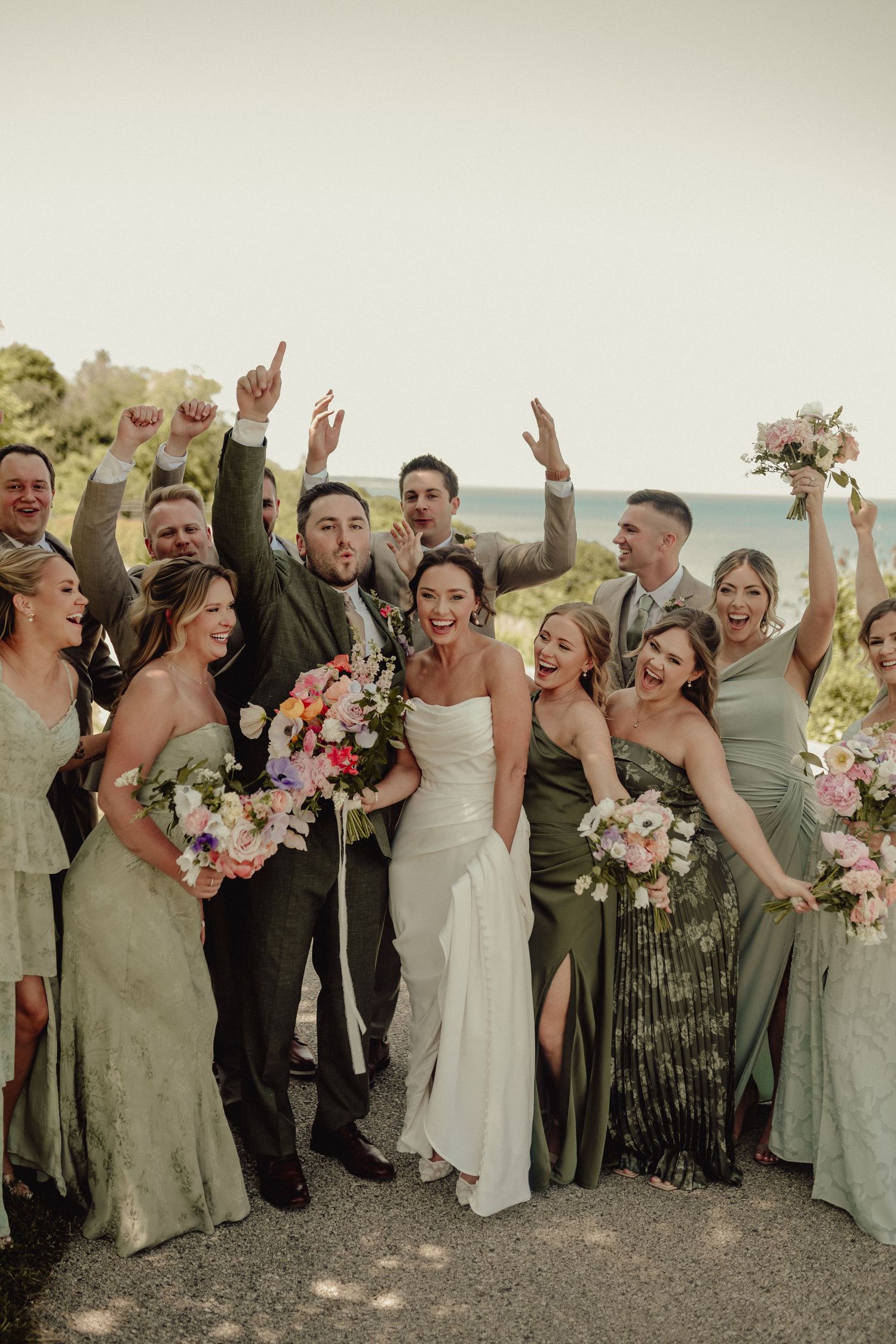 Wedding party in sage green and white attire celebrating outdoors.