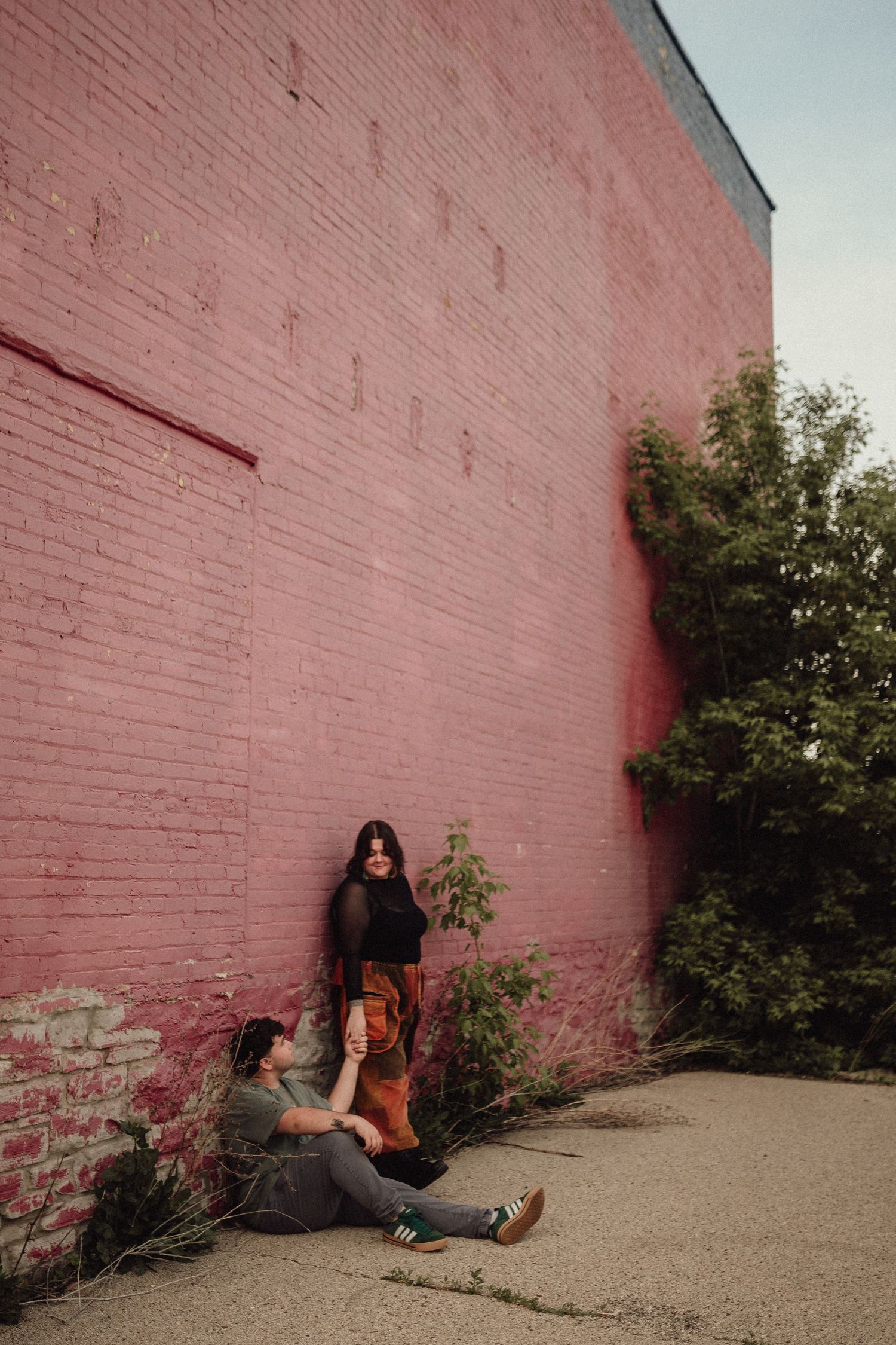 Casual couple's photoshoot with pink brick wall backdrop in urban setting.