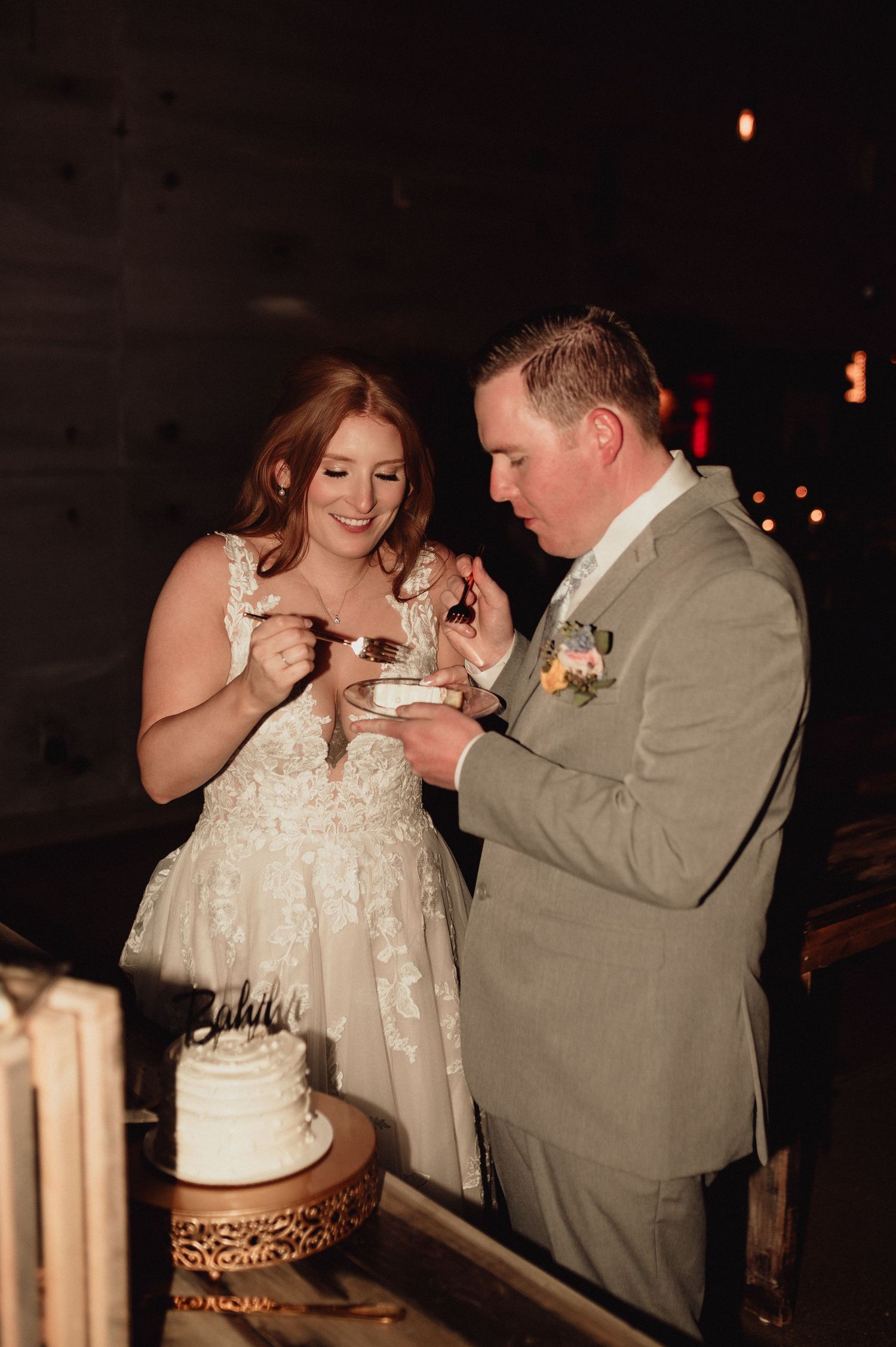 A couple playfully shares wedding cake during their reception in a dimly lit venue.
