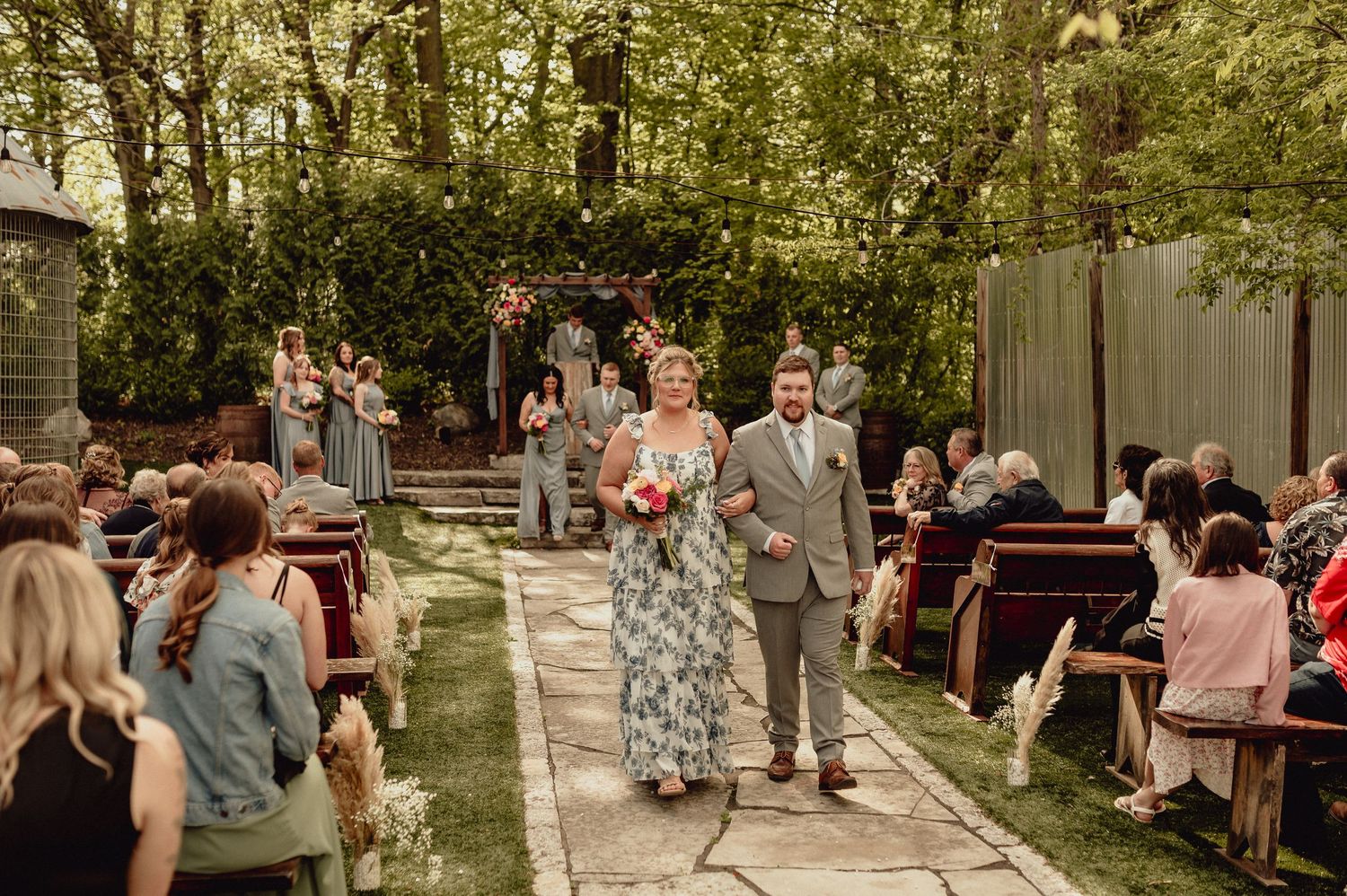 Wedding guests mingle and socialize in an outdoor garden setting during a sunny daytime celebration.