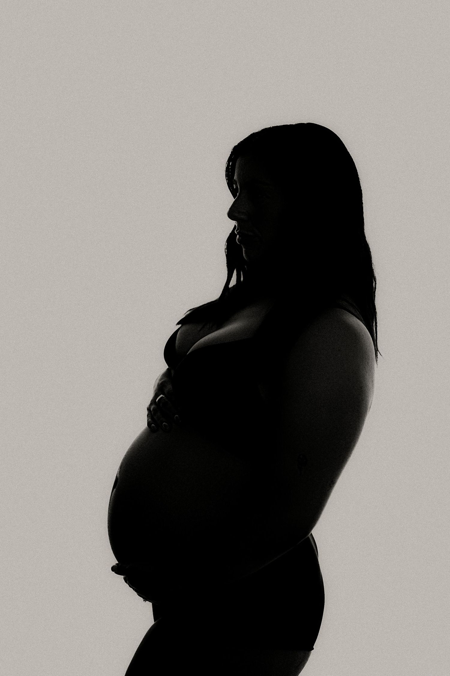Artistic silhouette portrait of pregnant woman against light background.
